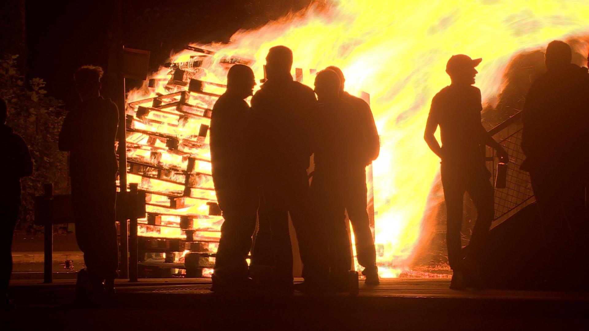 Men standing beside an Eleventh Night bonfire in Belfast