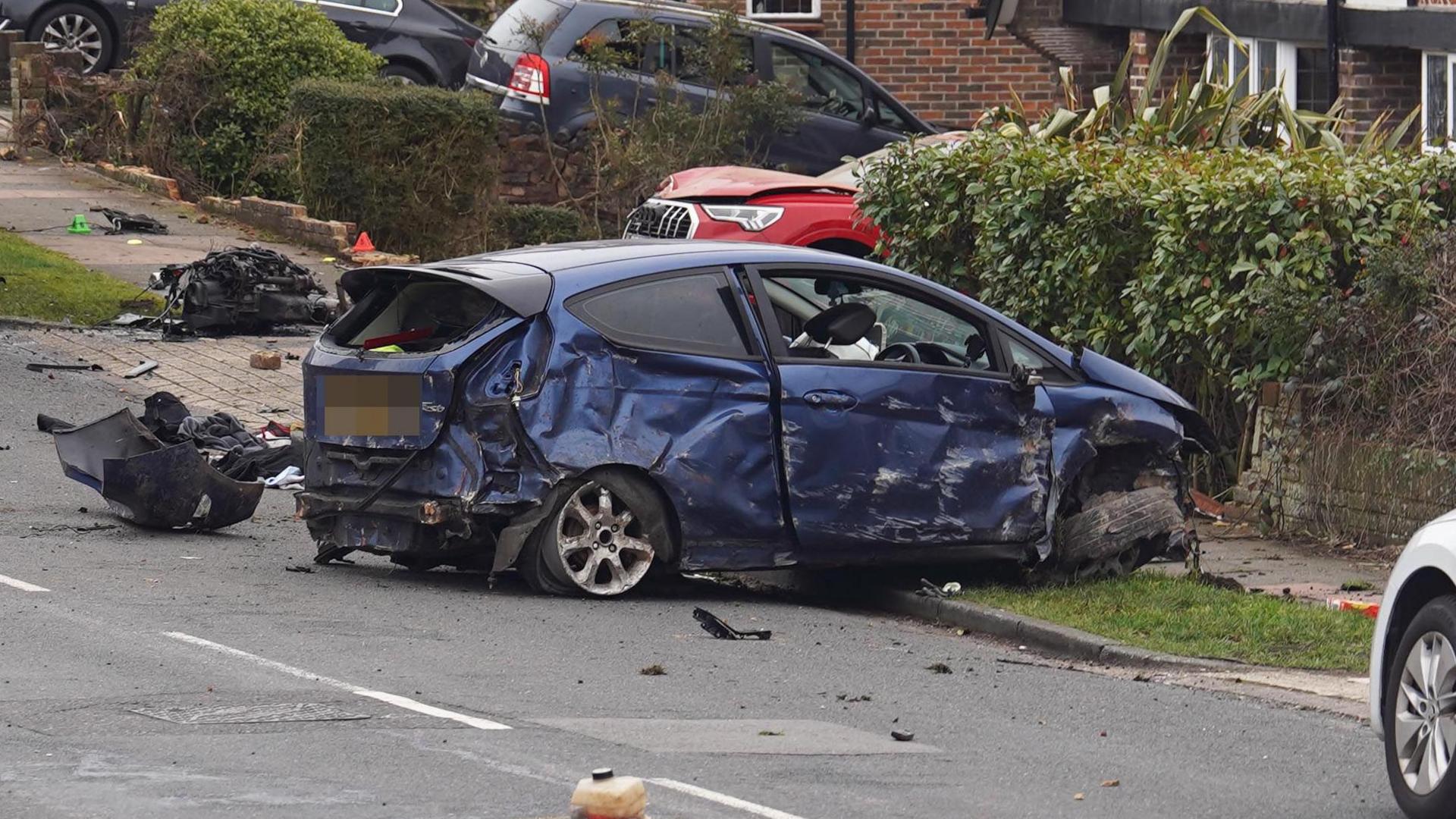 A navy car which is severely damaged and mounted on a path.