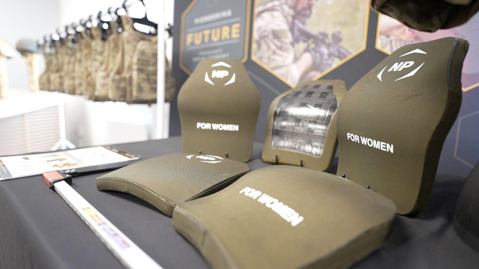 Curved and flat ballistic plates are displayed on a table next to each other for comparison.