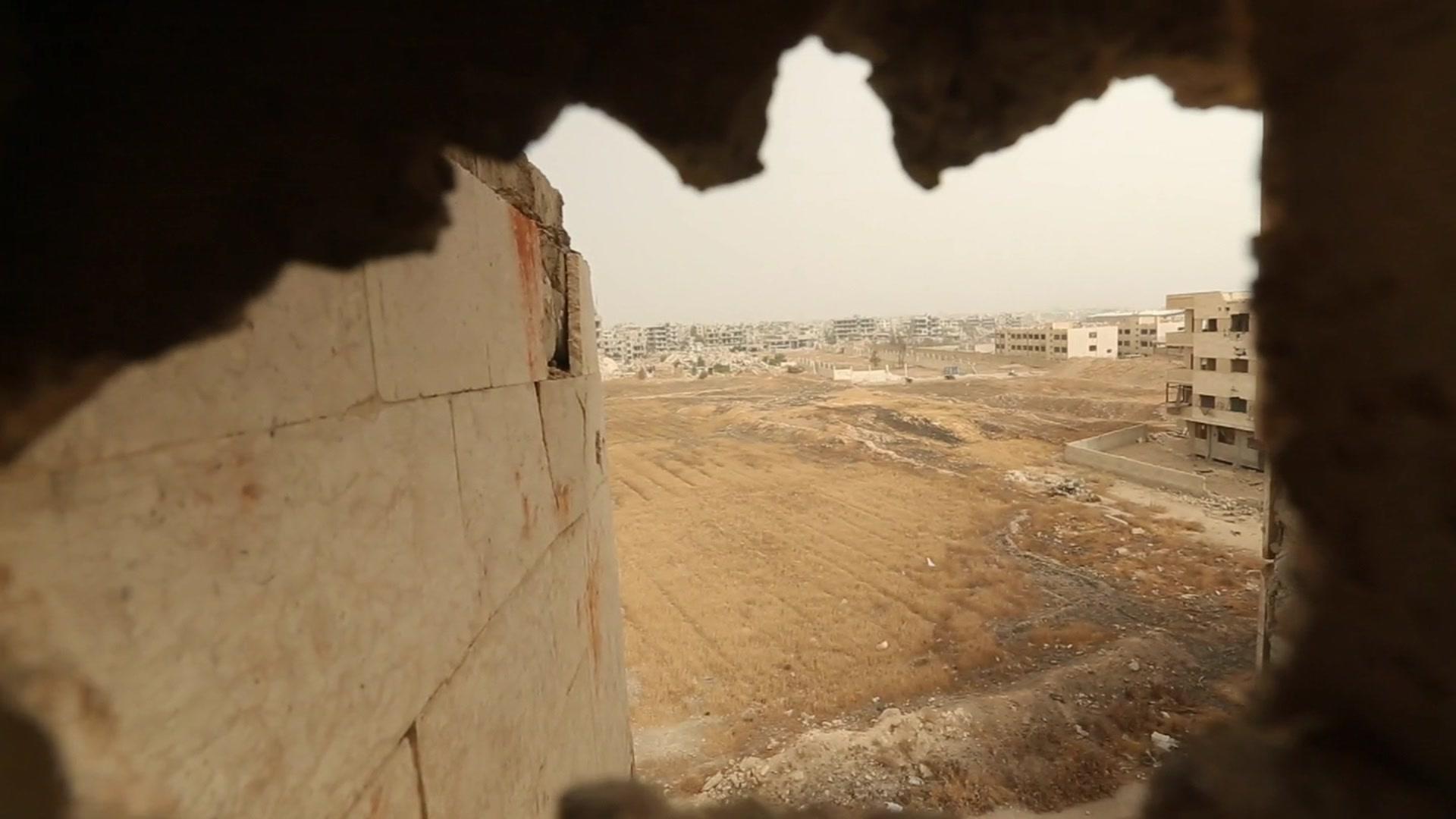 Camera looking through hole in wall to buildings outside