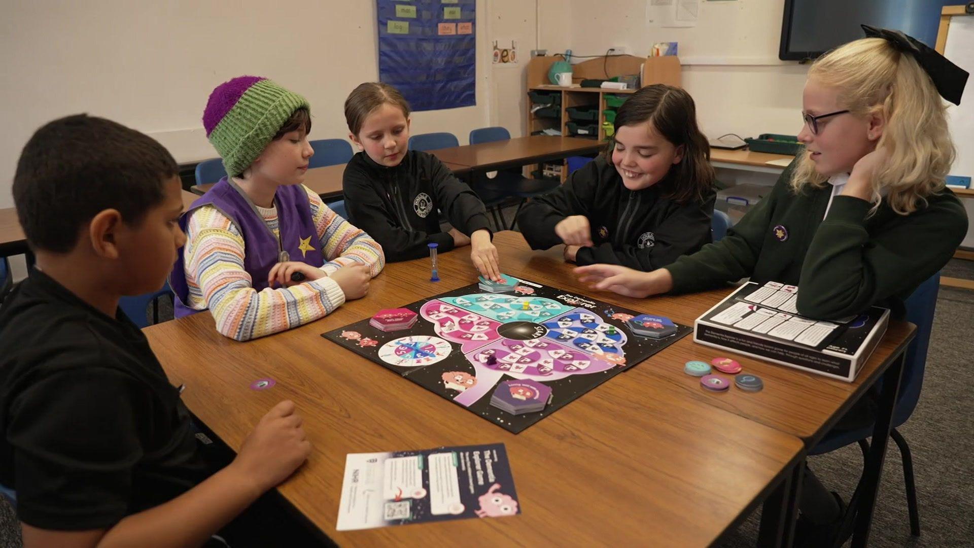 Five children sat around a table in a classroom playing a board game they helped to design