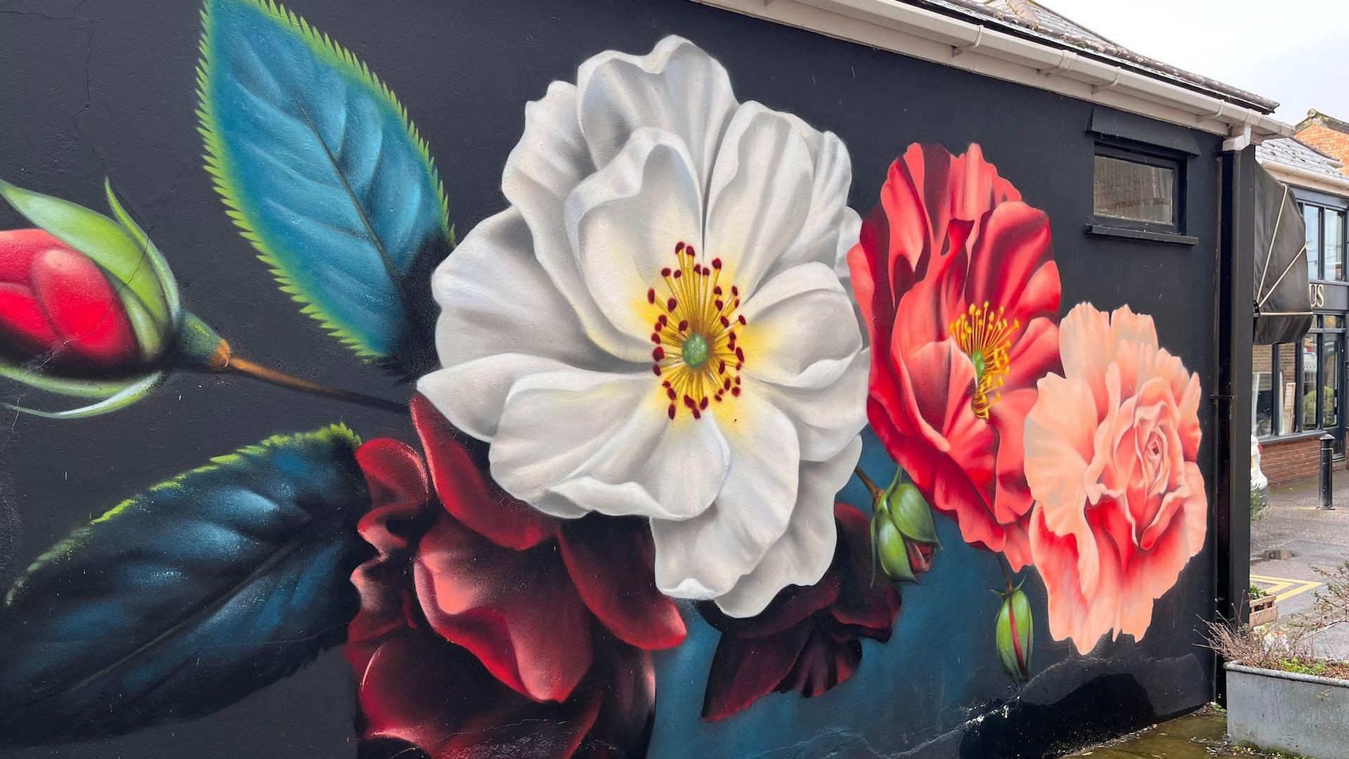 Giant white, red and pink flowers are painted on to the side of a building, with a black and dark blue background
