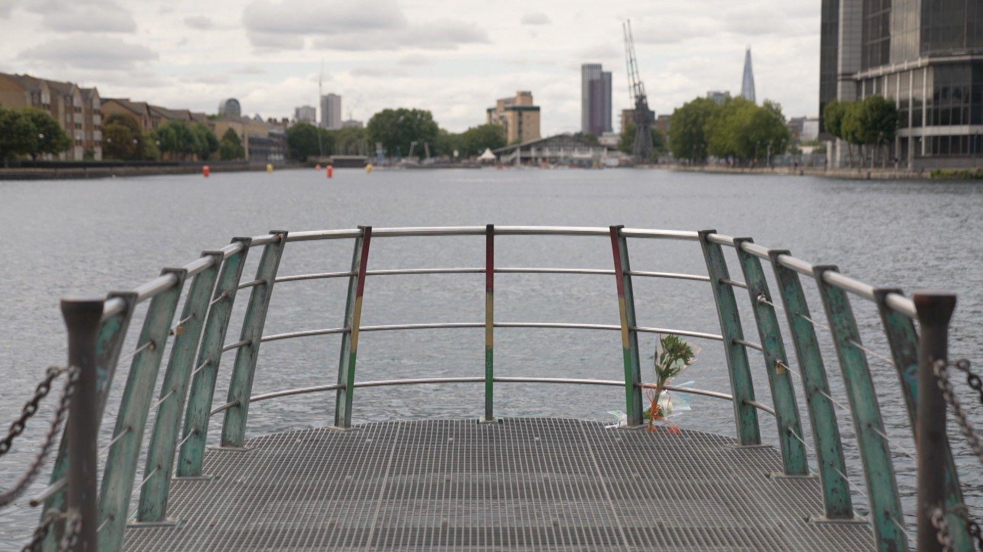 A dockland area with housing and boats at the quayside with flowers tied to the railing. 