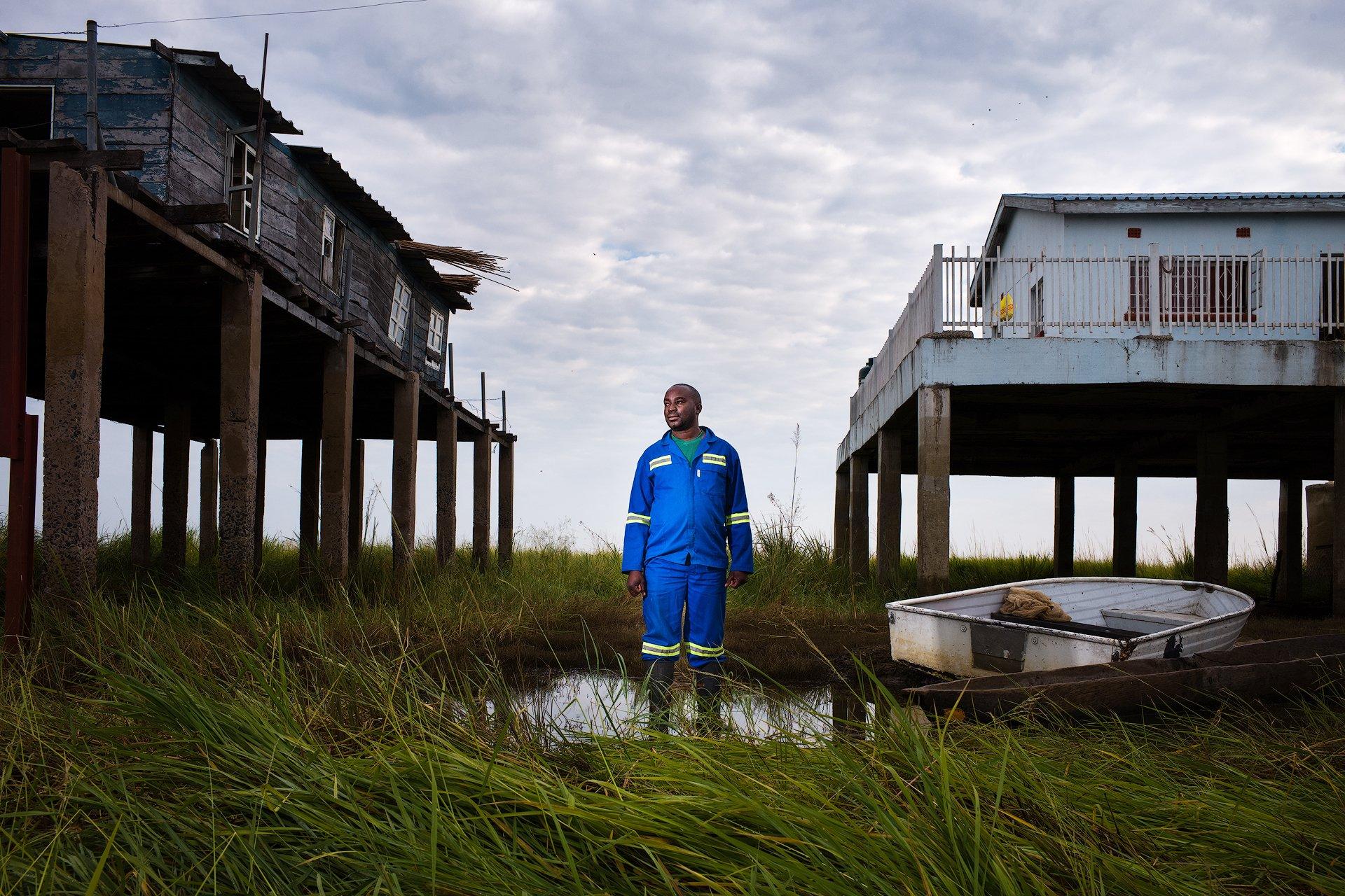 man stood between 2 homes on stilts. One higher up than the other