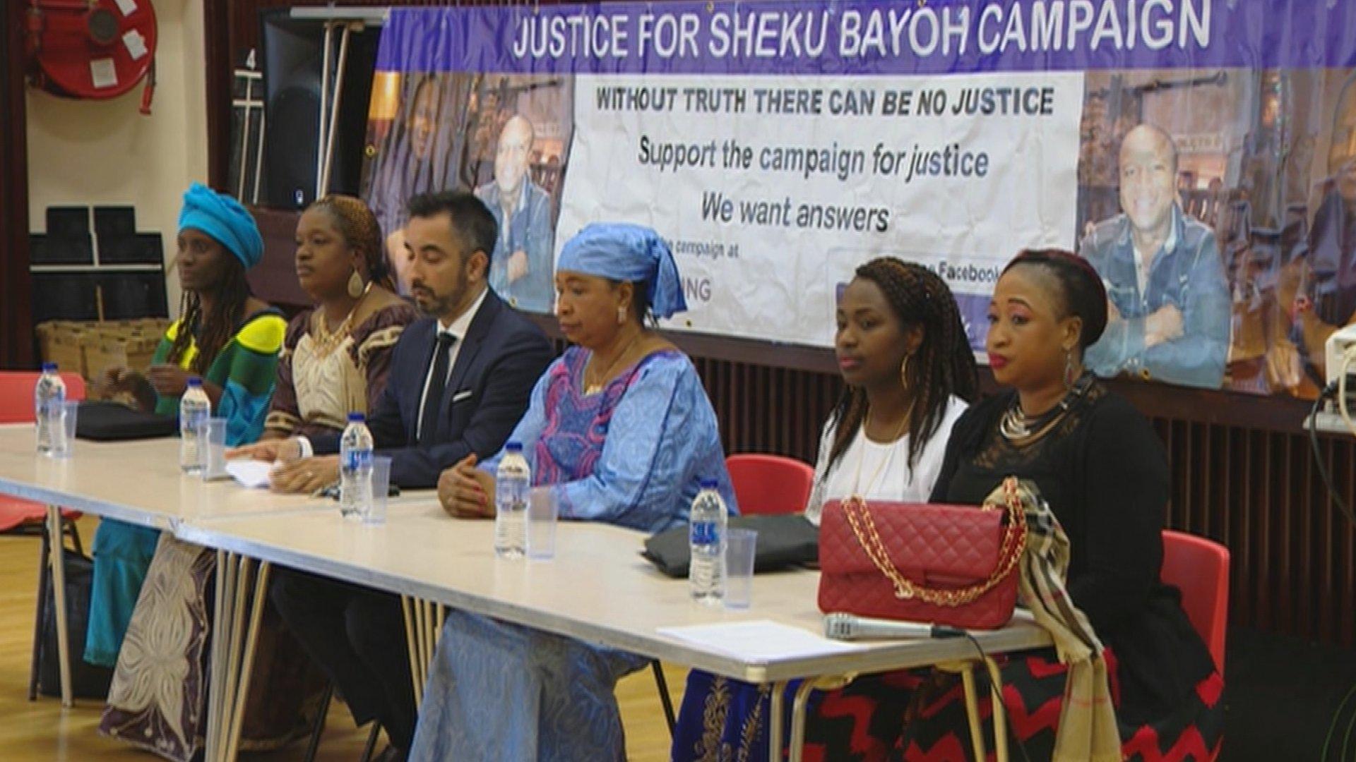 Relatives of Sheku Bayoh sit in front of a banner with slogans campaigning for justice, after a memorial service in Kirkcaldy, Fife.