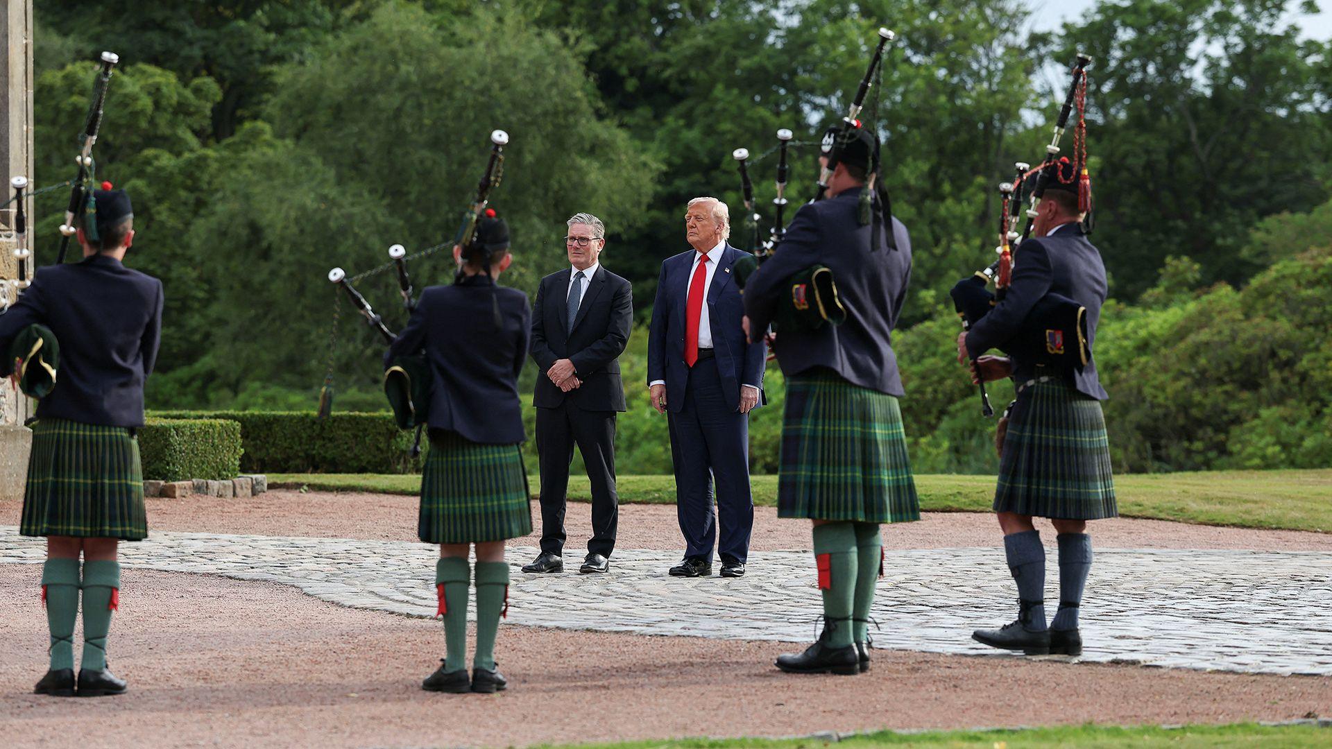 Donald Trump and Keir Starmer stand surrounded by bagpipers and greenery