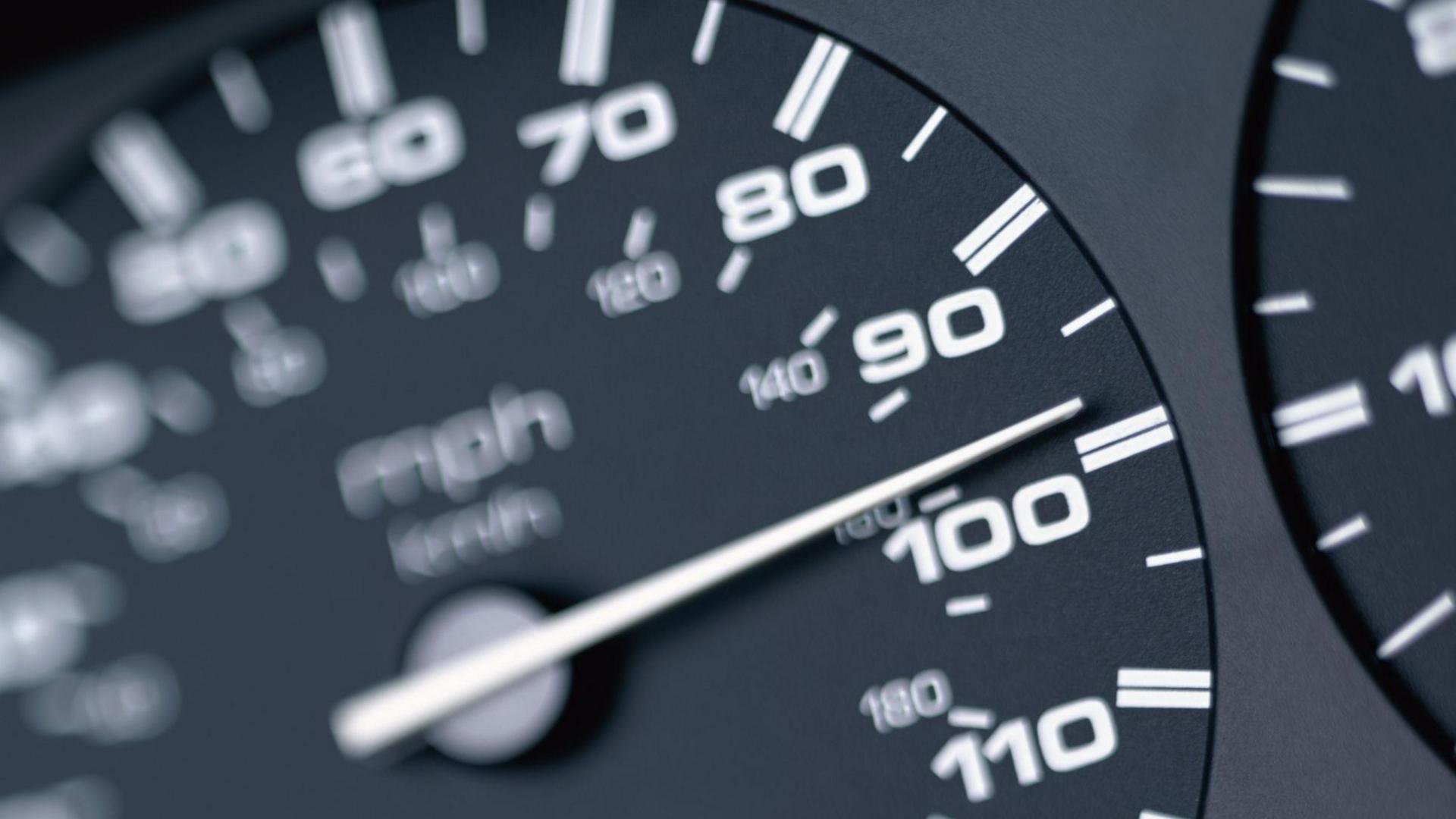 A black and white car speedometer showing a speed of just under 100mph. 