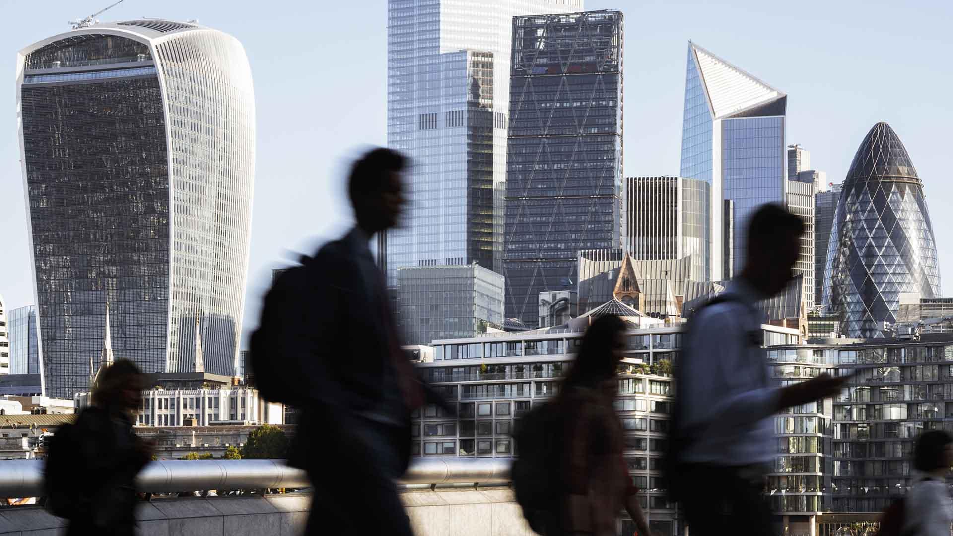 People in silhouette walking by the bank of the Thames, with skyscrapers in the background