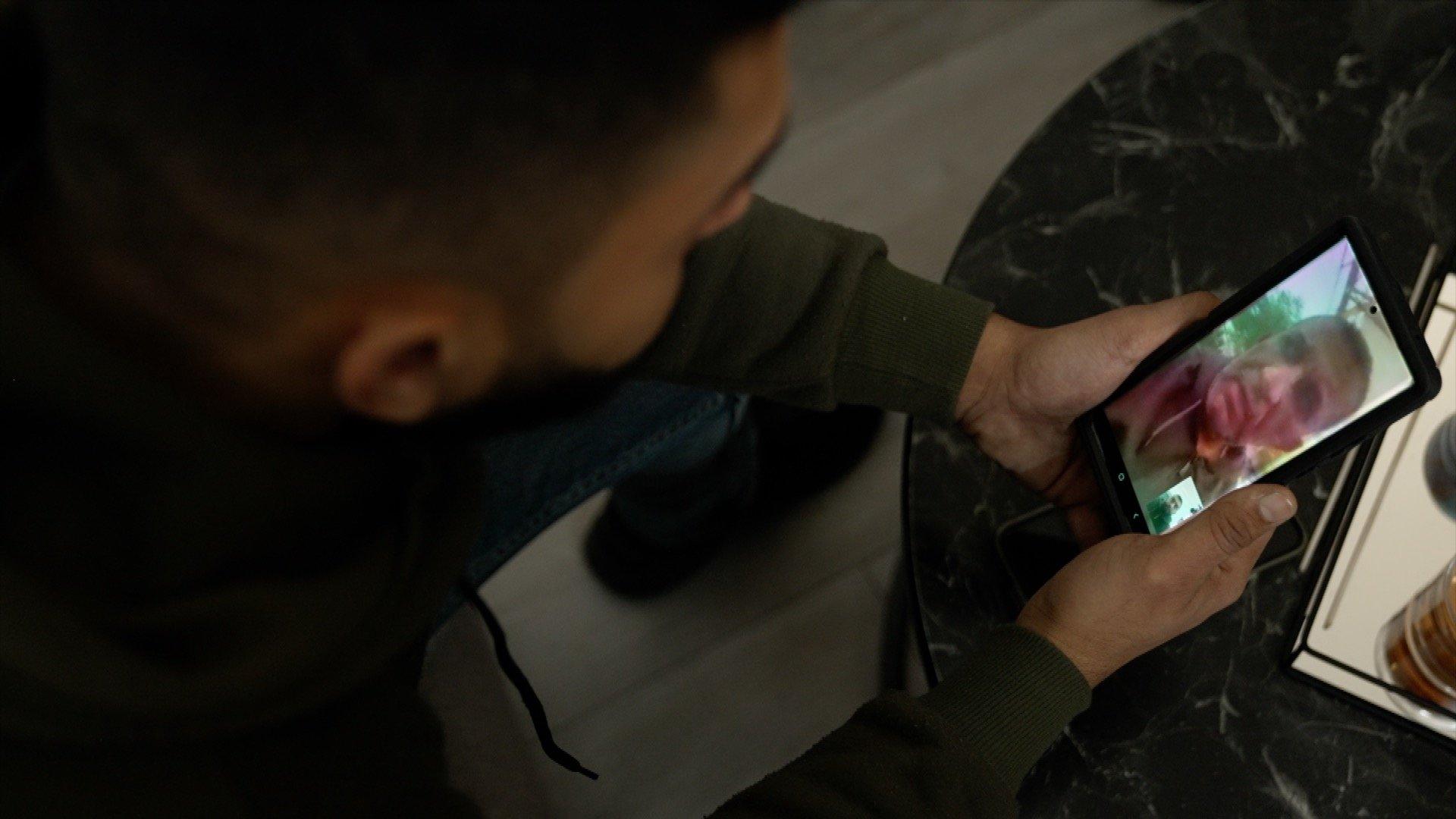 Jawdat Mikhael holds his phone while he speaks with his father, on videocall