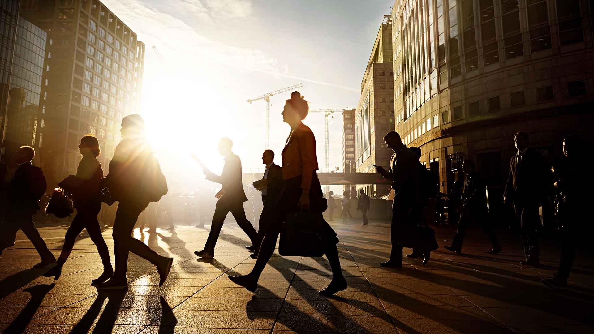 People in outline walking through city of London at sunrise