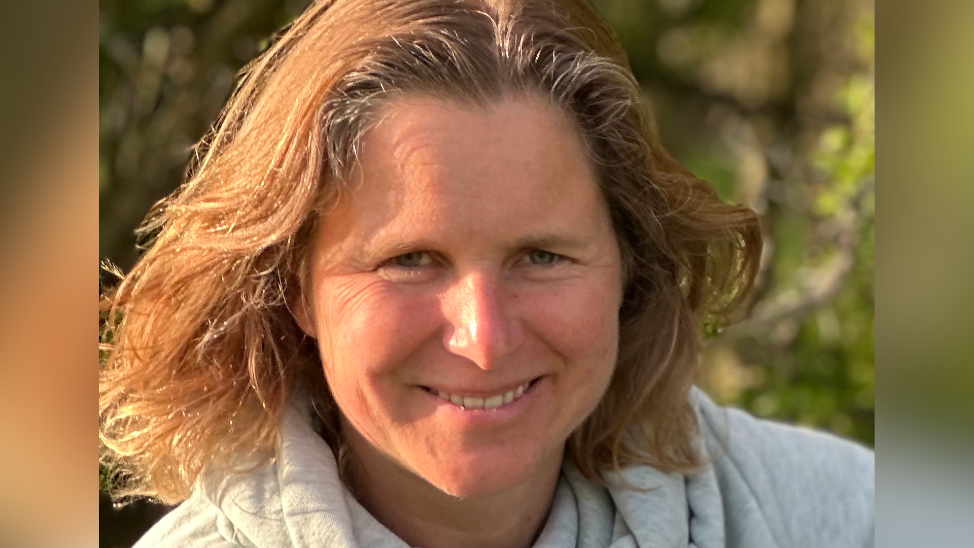 Dr Keith is smiling at the camera while outside. The sun is shining on one side of her face. She has medium length brown hair and is wearing a grey jacket.