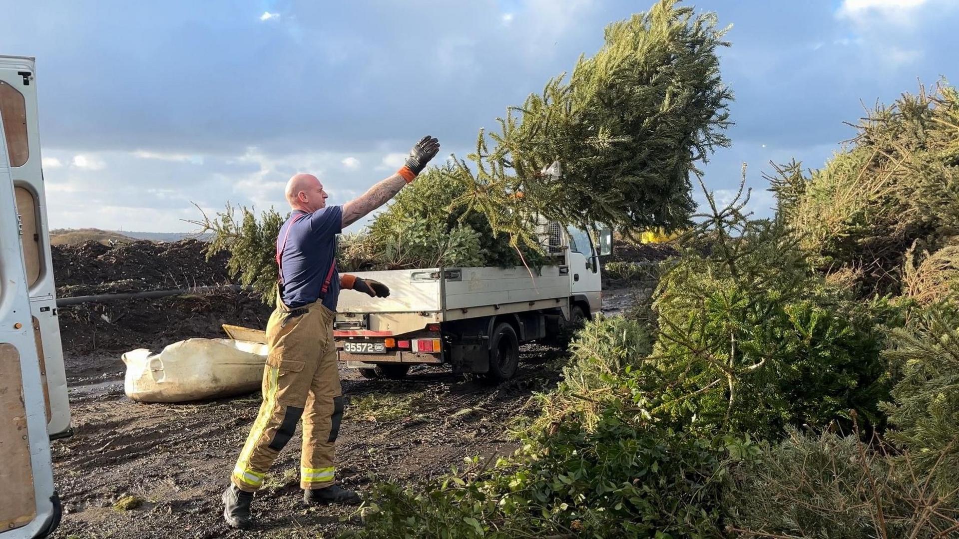 Fireman throws tree onto larger pile of trees. 