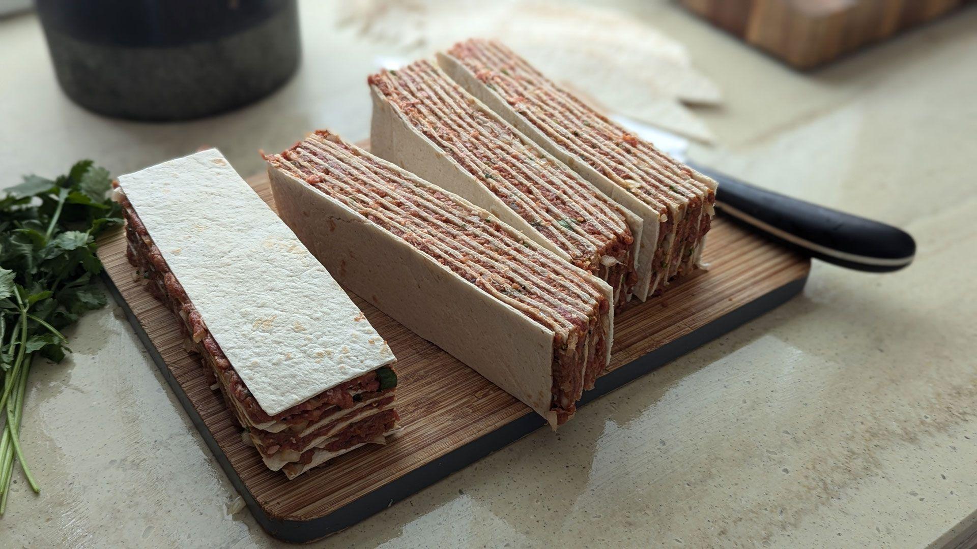The mince spread on multiple layers of the wraps, with wraps at both ends too. There are four large blocks of the kebabs on a chopping table waiting to have skewers put through them