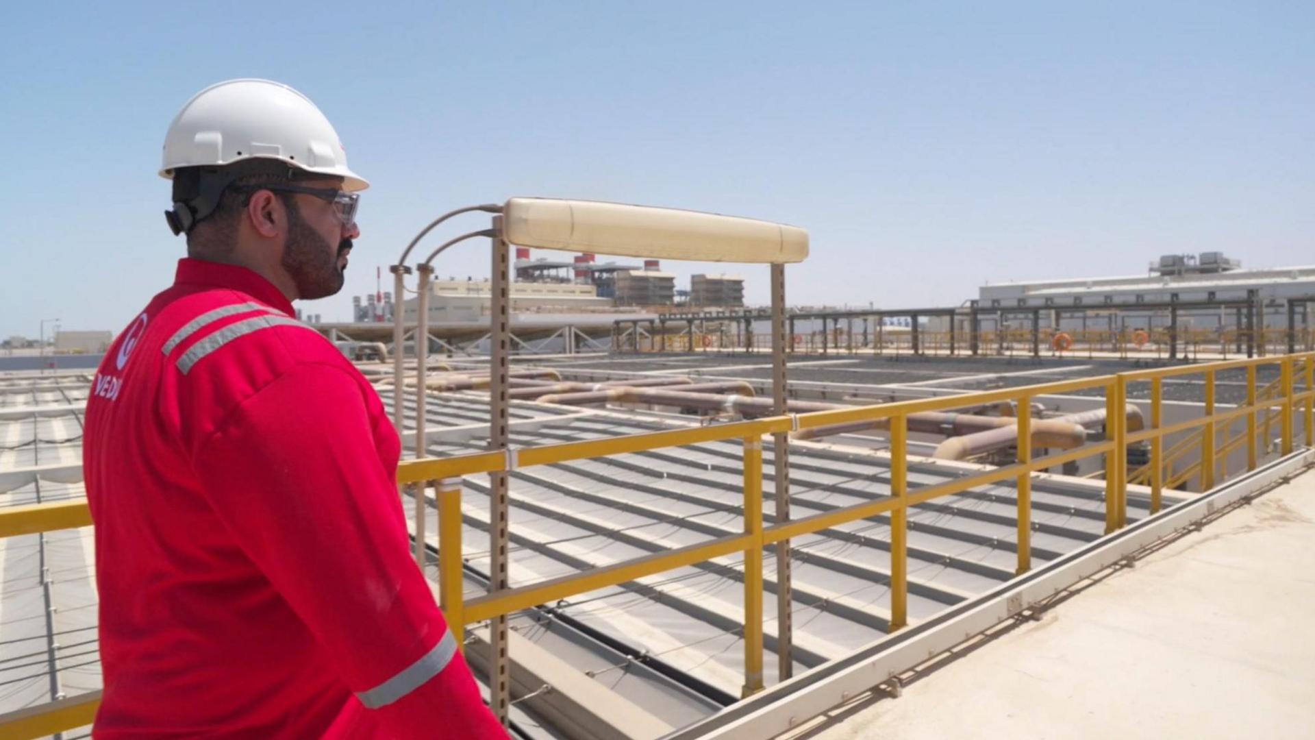 A man in red high-vis jacket is on a walkway through a huge desalination plant in Oman.