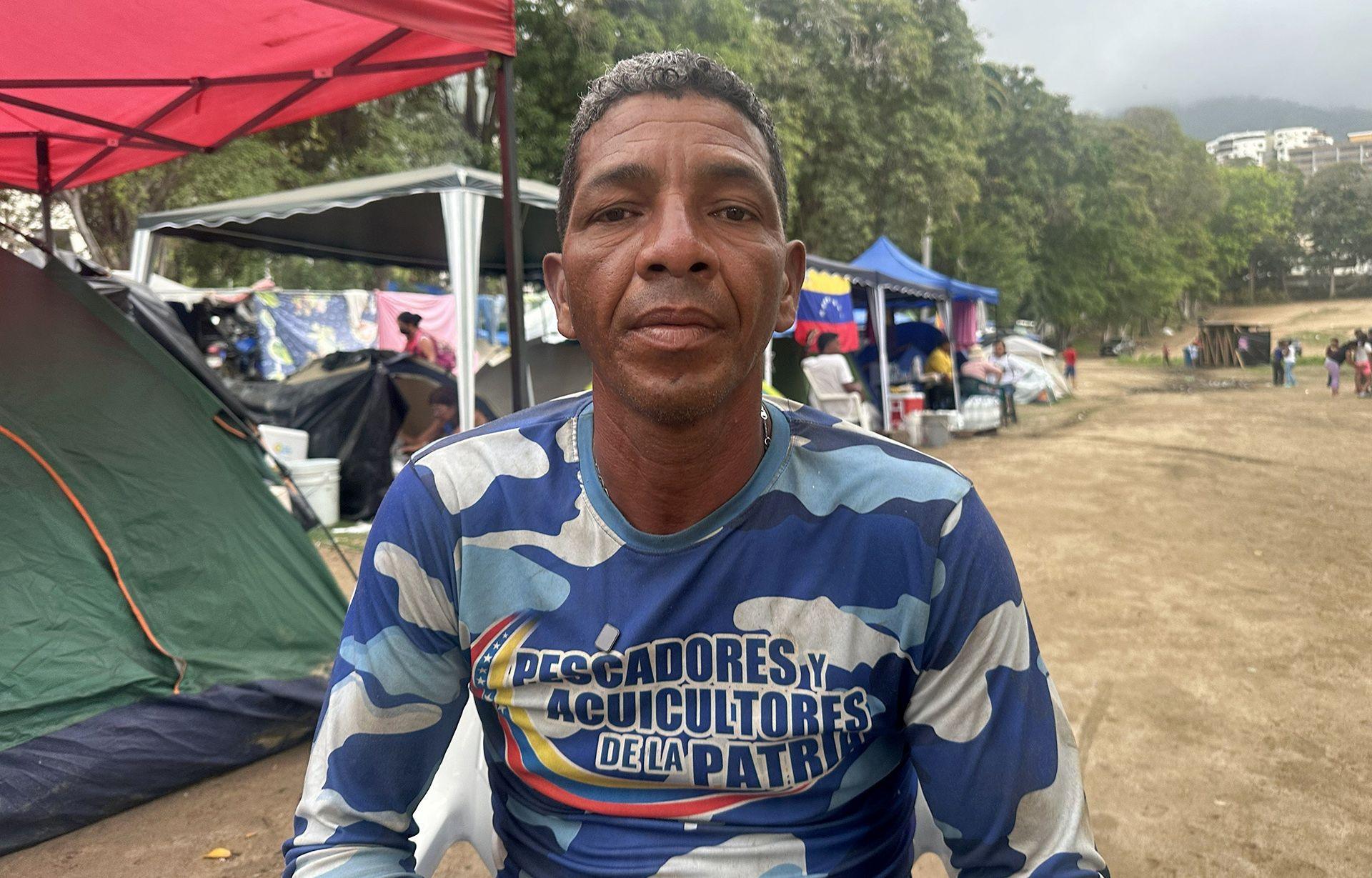 Victor Calderón wearing a blue T-shirt, sits among a row of tents on a golf course which is now his home after the building he lived in collapsed.