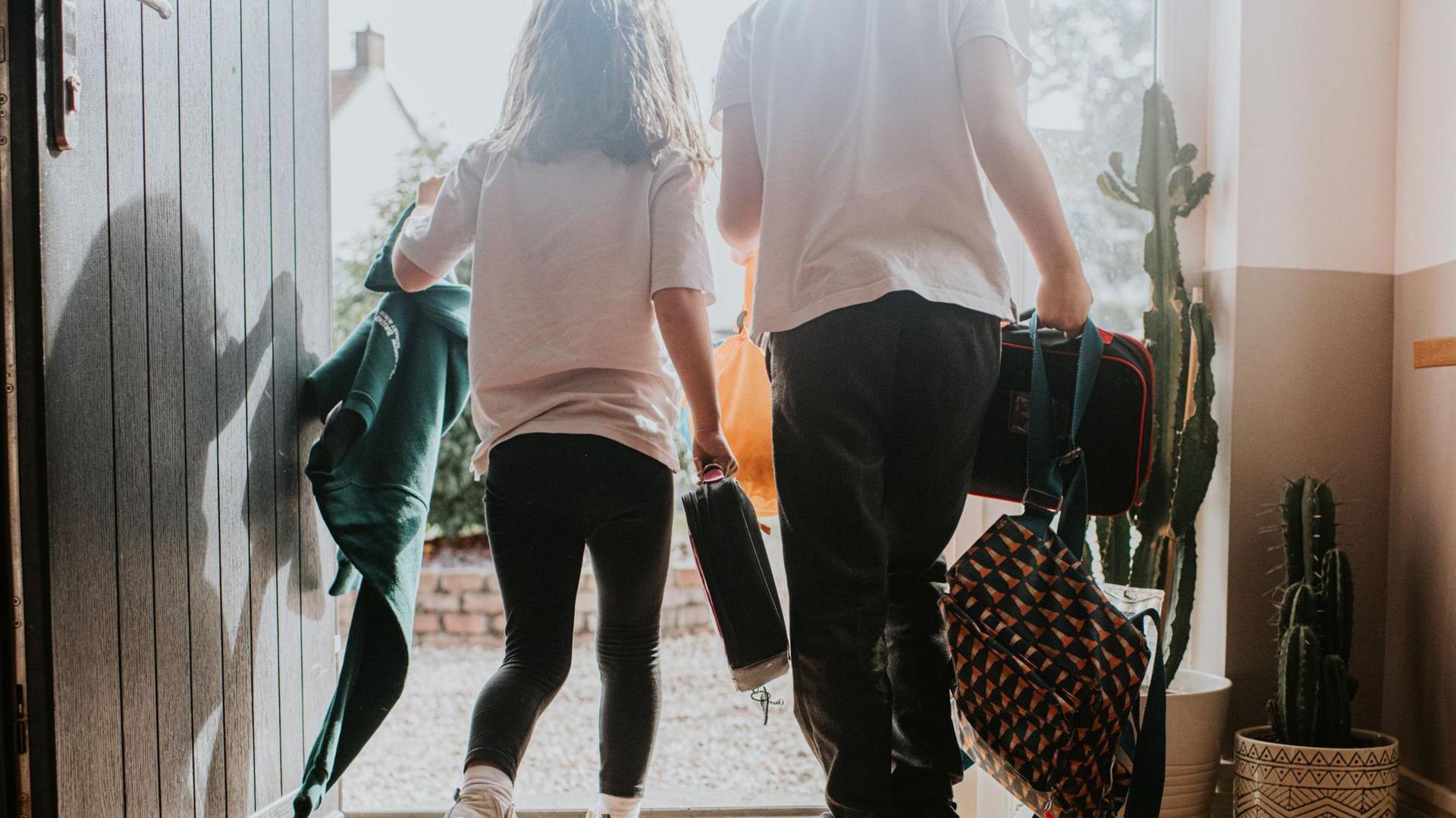 Children leaving the front door in school uniform, carrying bags 