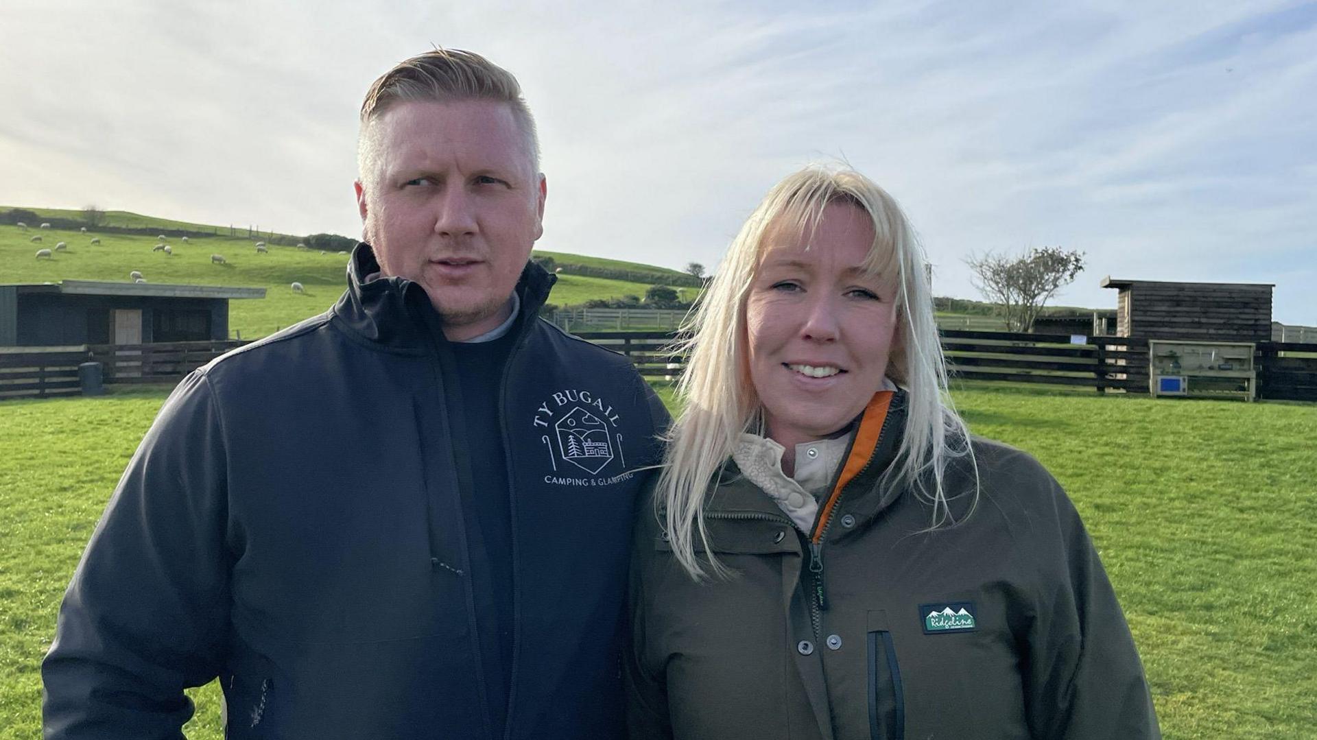 Luke Haworth wearing black jacket on left, with partner Samantha Fielding on right, with long blond hair and wearing a green and orange waterproof coat