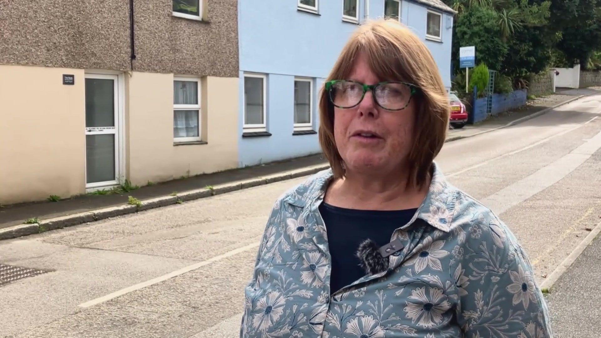 Carol Wilson, with shoulder-length brown hair and glasses, in front of road