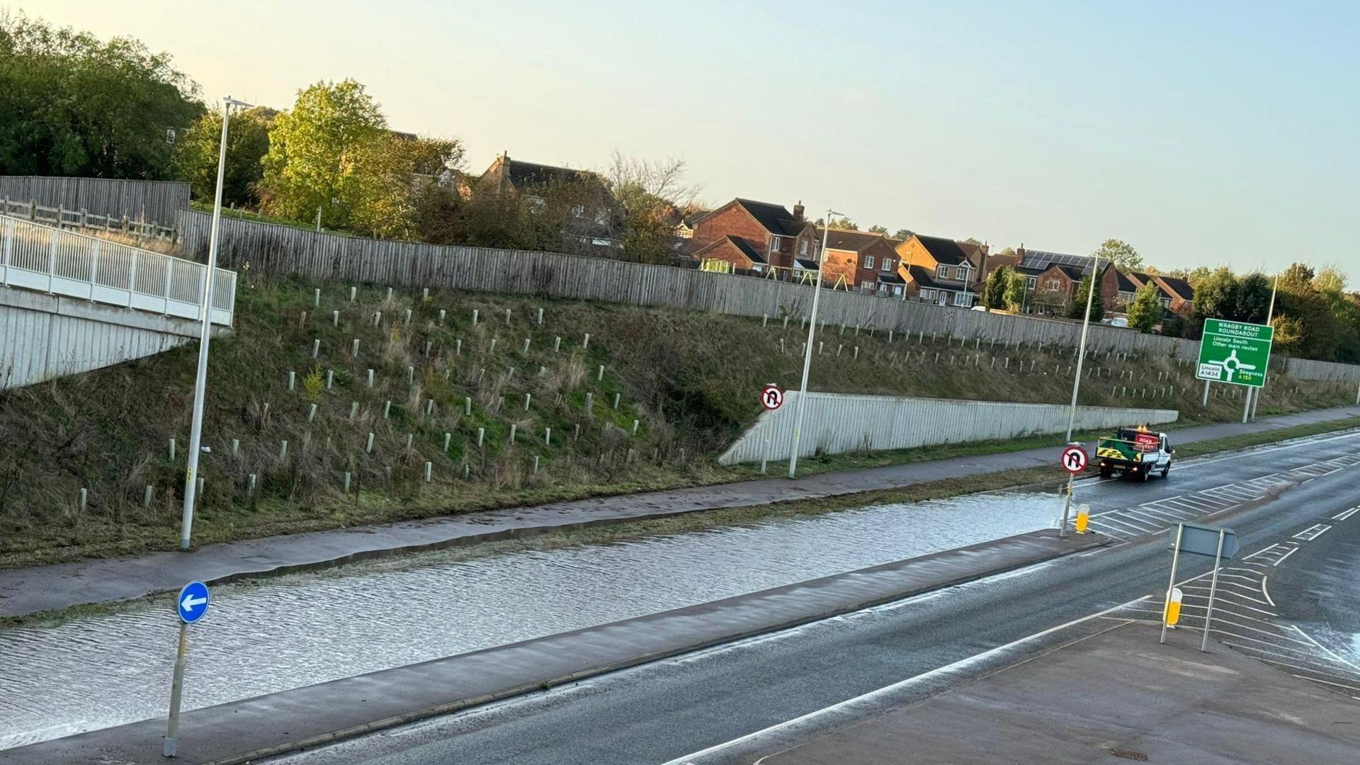 An image of the flooded Lincoln Eastern Bypass. Standing water can be seen in the northbound lane and a grass embankment is visible in the background. A highways maintenance van is also parked close to the water on the right of the image.