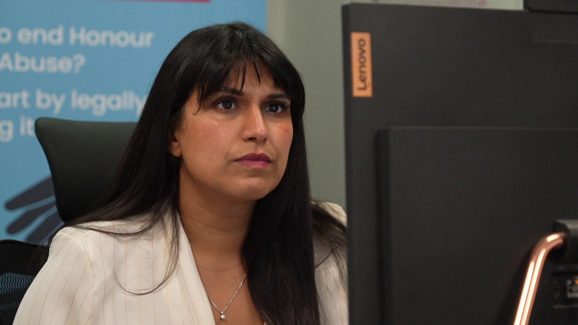 A woman with brunette hair and bangs looks at a computer screen.