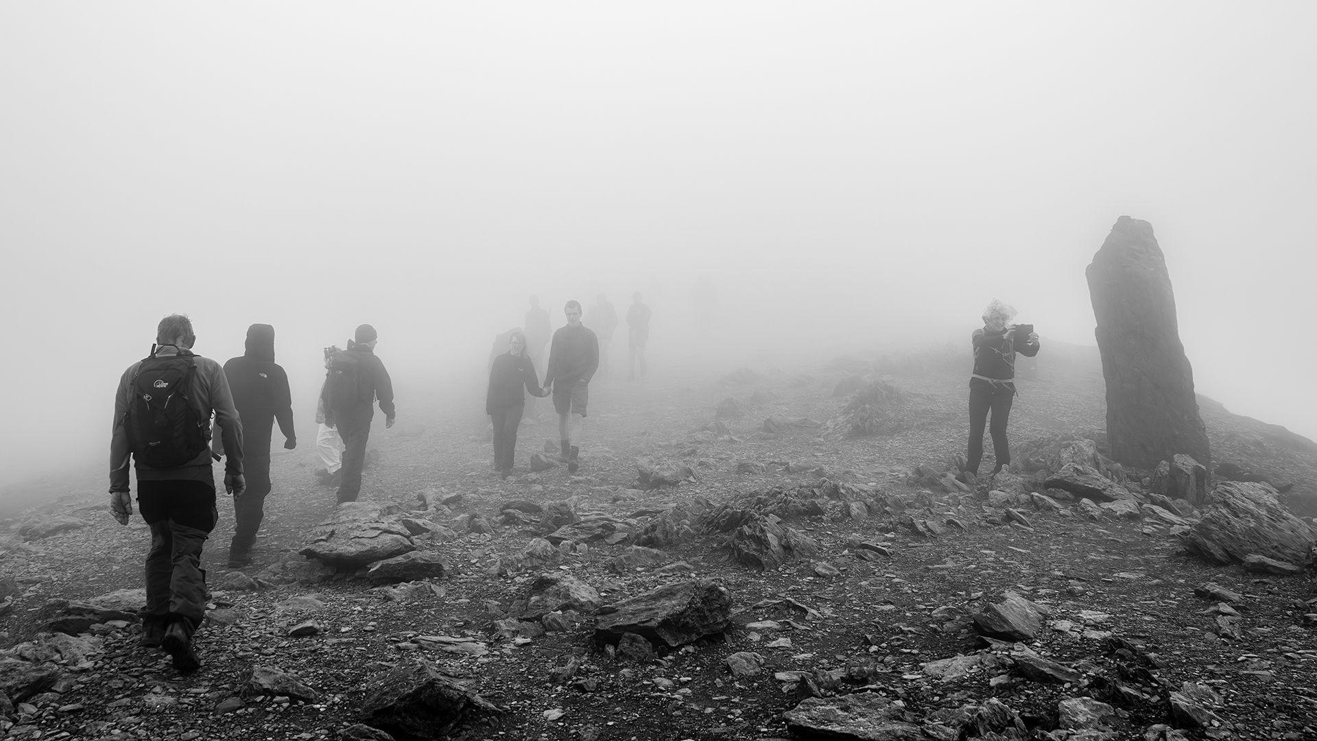 Pobl yn cerdded wrth gopa'r Wyddfa yn y niwl