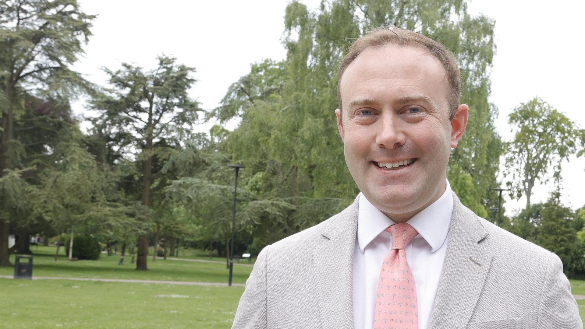 A picture of Conservative MP Blake Stephenson, who is stood in a park. He is wearing a light grey suit jacket and a pink tie and white shirt.