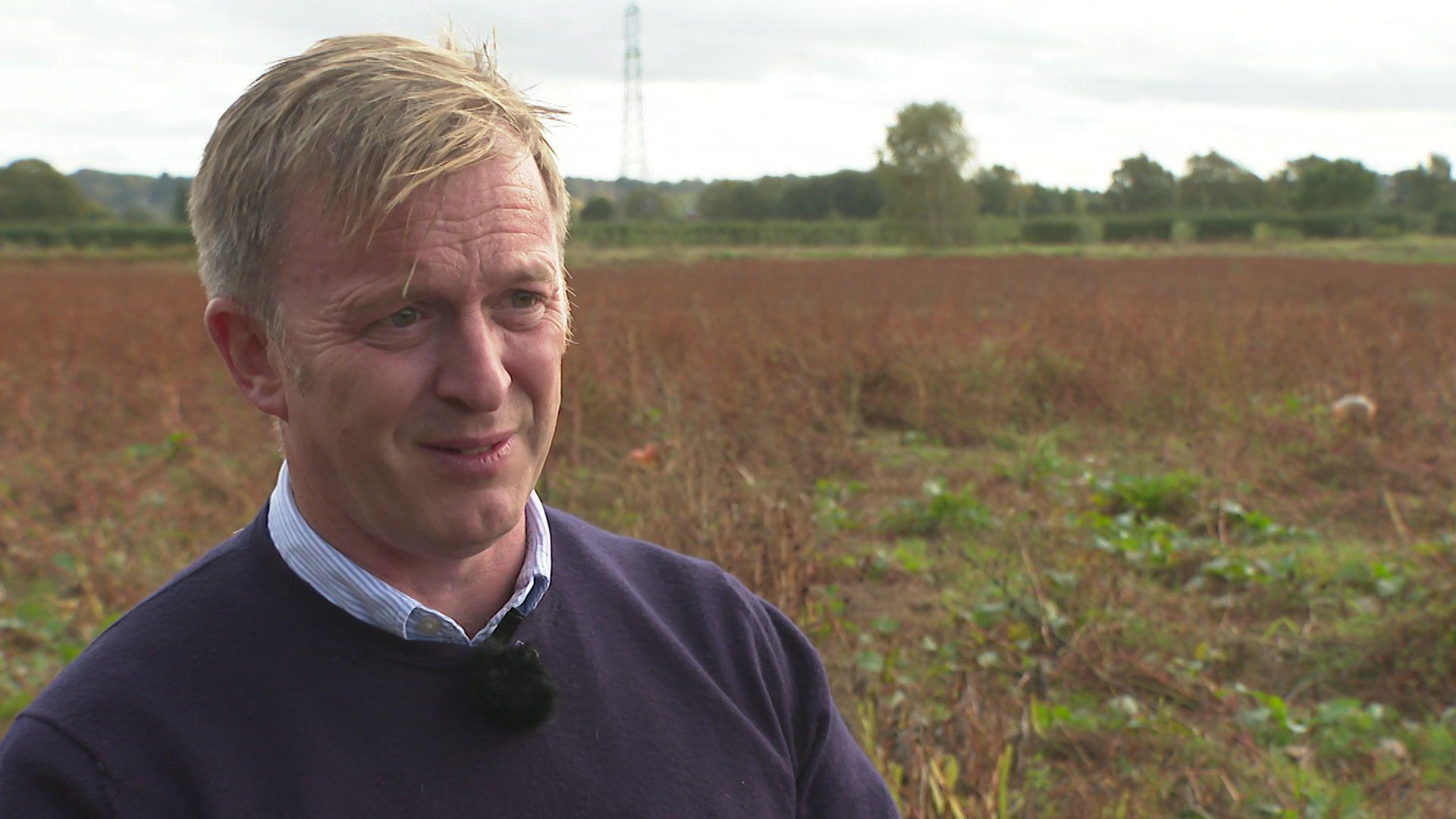 Farmer Jonathan Hewitt, who is wearing a purple jumper, is standing in front of an empty field