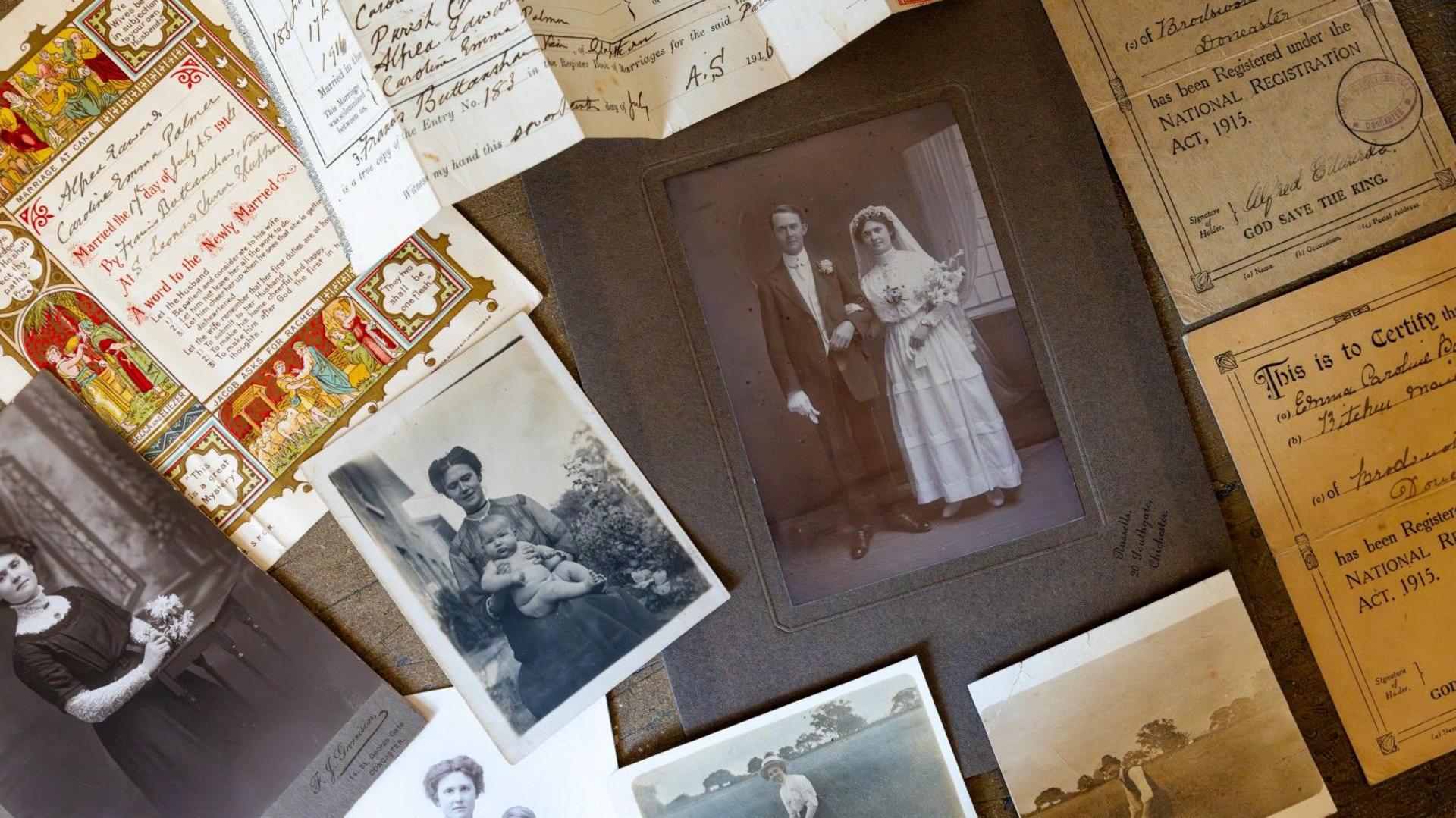 A number of old black and white photos, of a young woman, one showing her with two young boys and one of a wedding photo of her. They are laid on a grey background, surrounded by yellowing documents including a wedding certificate