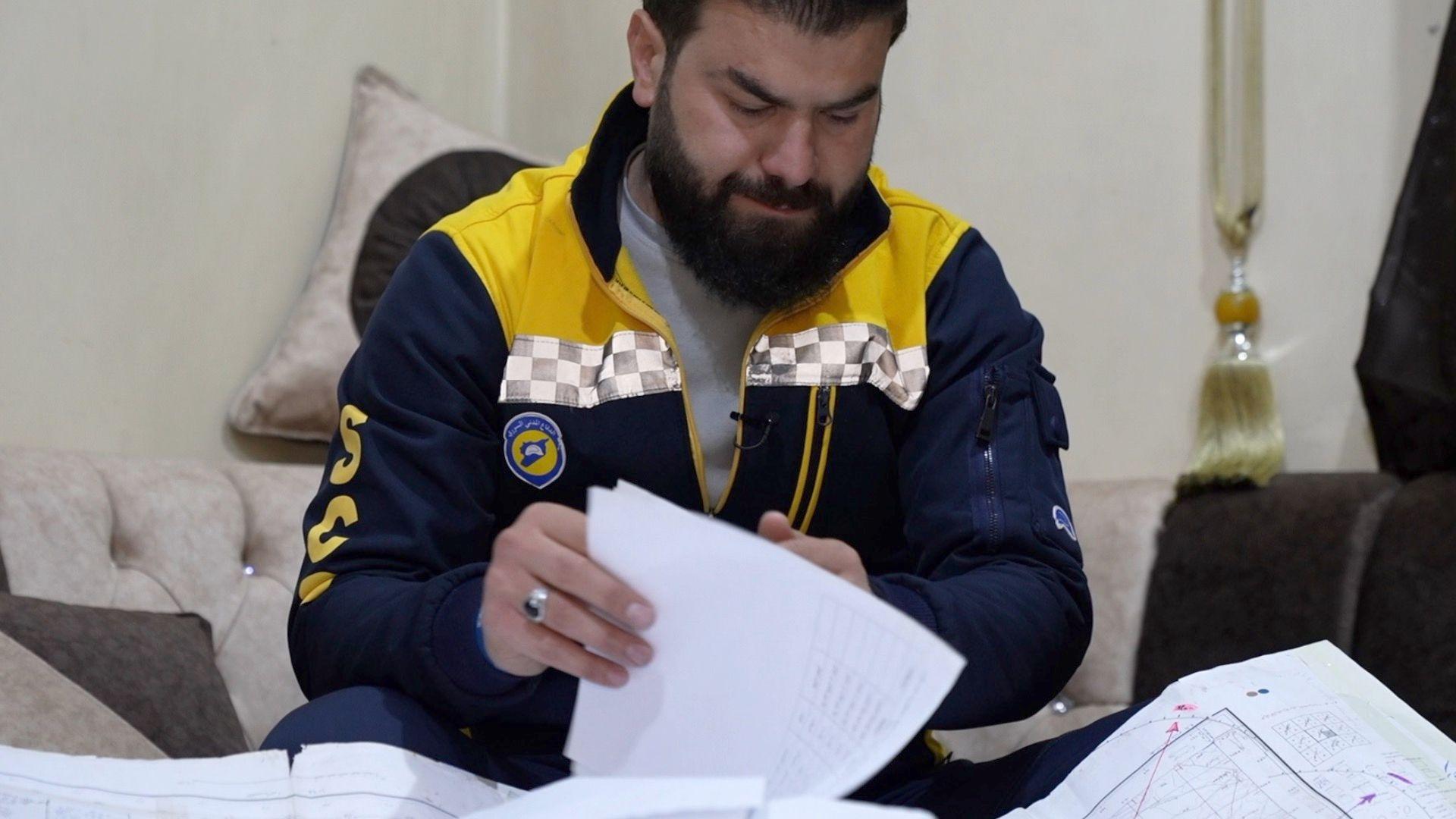 Man wearing White Helmets uniform - navy blue and yellow - looking through documents and maps. 