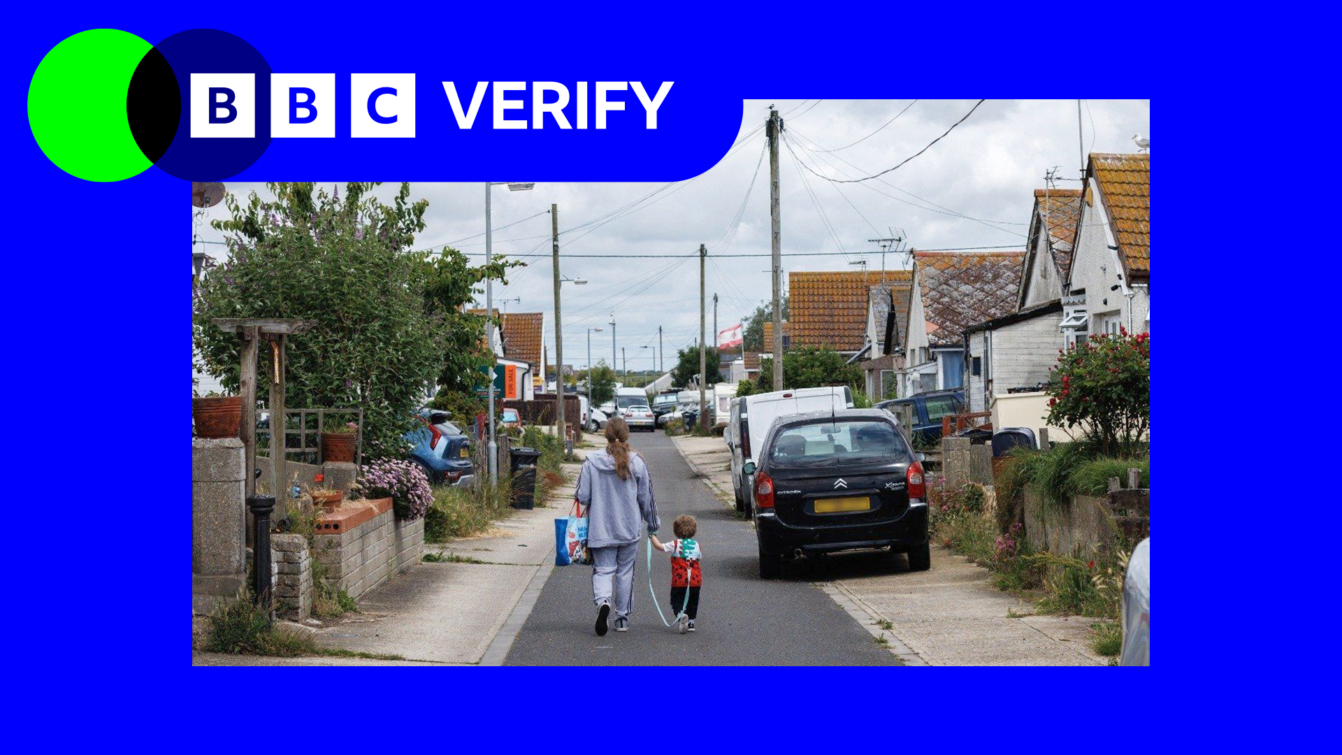A photo of a woman and a young child walking down a residential street with cars parked on the pavement on either side. The street is lined with houses and overlooked by low telephone lines. The sky above is grey. The photo has a blue border with a green and blue BBC Verify logo in the top left corner.