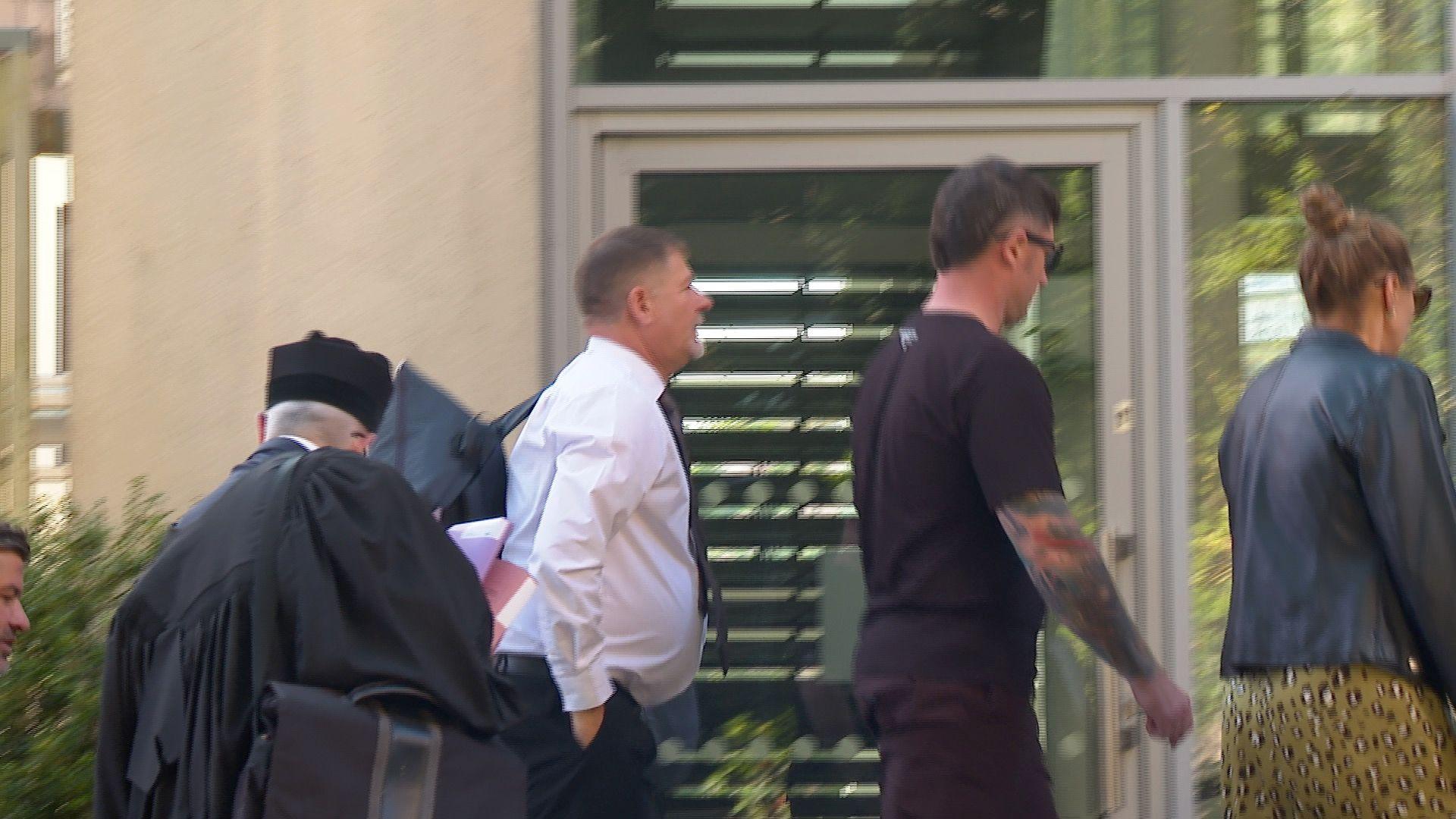 A group walking into Guernsey's Royal Court. In the centre is Jason Tardif, a man with black hair a grey beard wearing a white shirt and a navy blue tie.