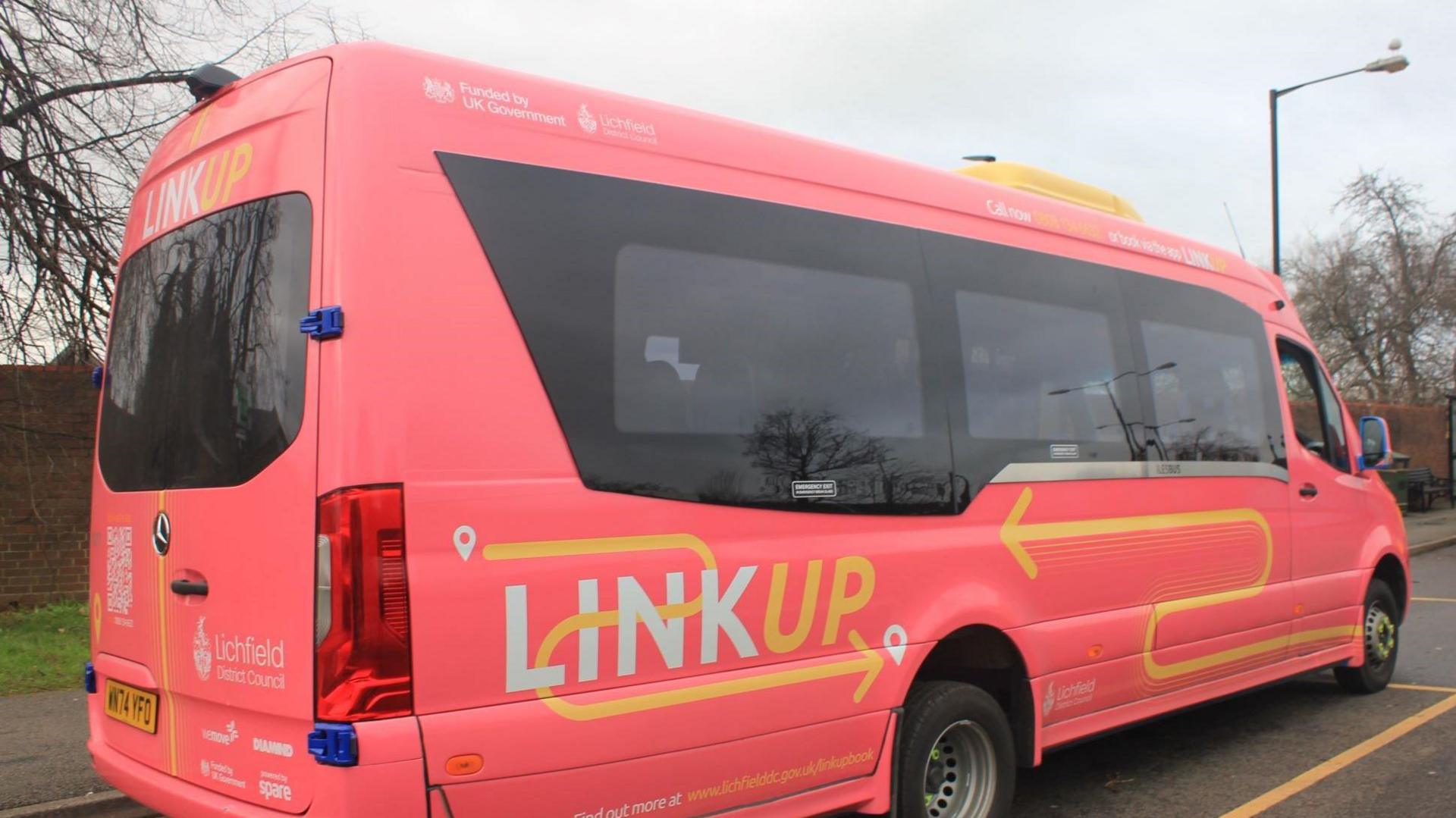 A pink-coloured mini bus with white and yellow lettering which reads 'link up' as well as the logo of Lichfield District Council.