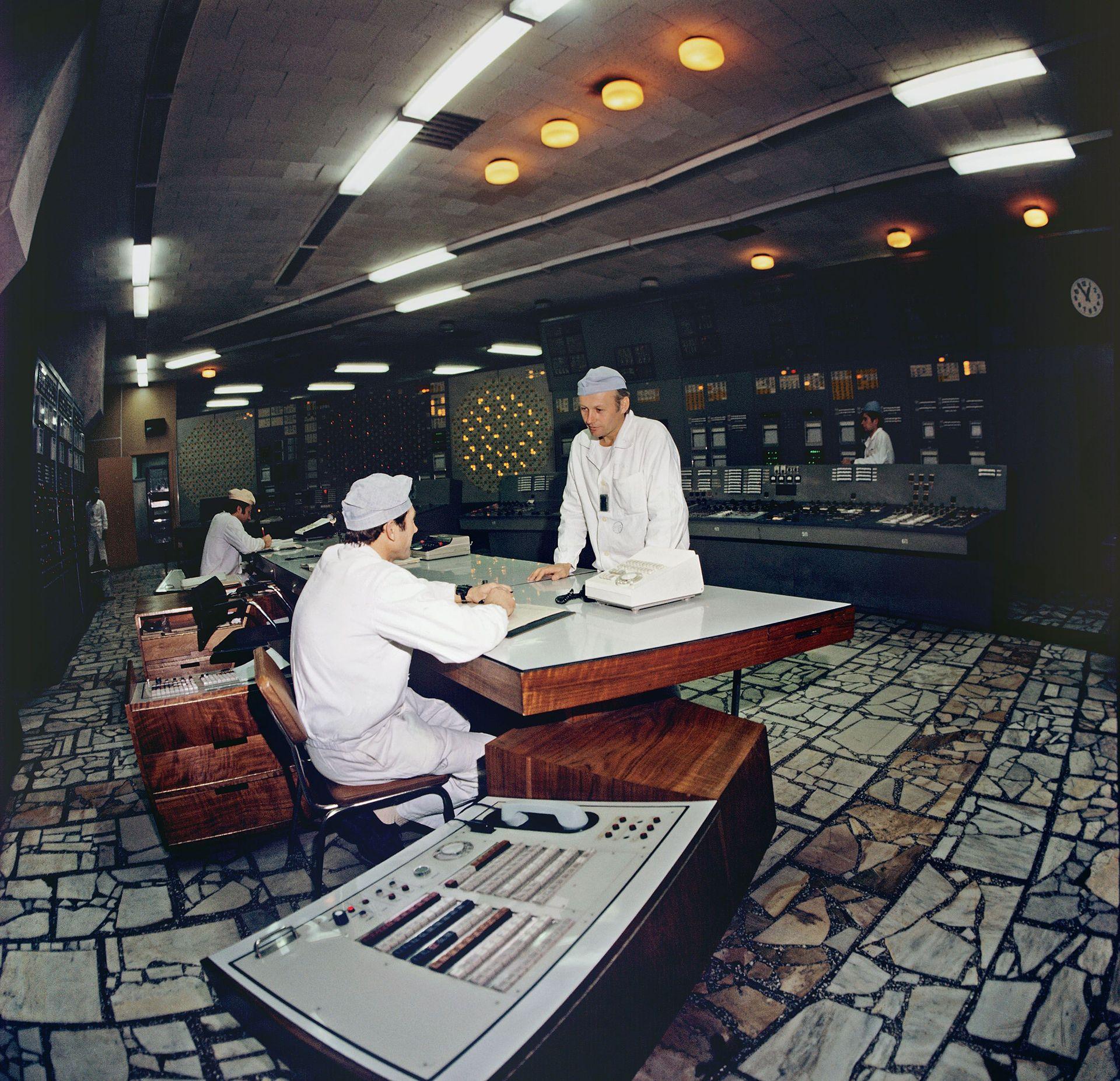 Archive colour image showing two workers in white suits and hats at a unit control desk at the Chernobyl Nuclear Power Plant in April 1983.