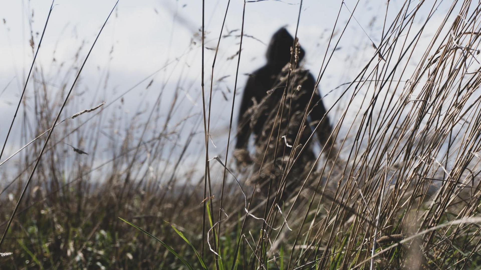 A man dressed in a black hooded top stands in a field