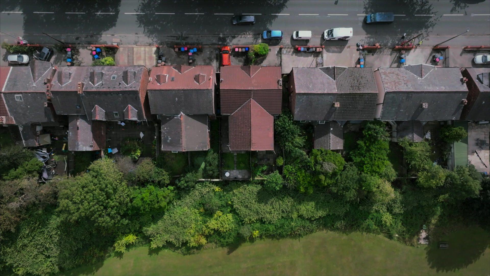 An aerial, birds-eye-view image of a row of Victorian style semi-detached houses backing onto dense undergrowth bordering a rugby pitch