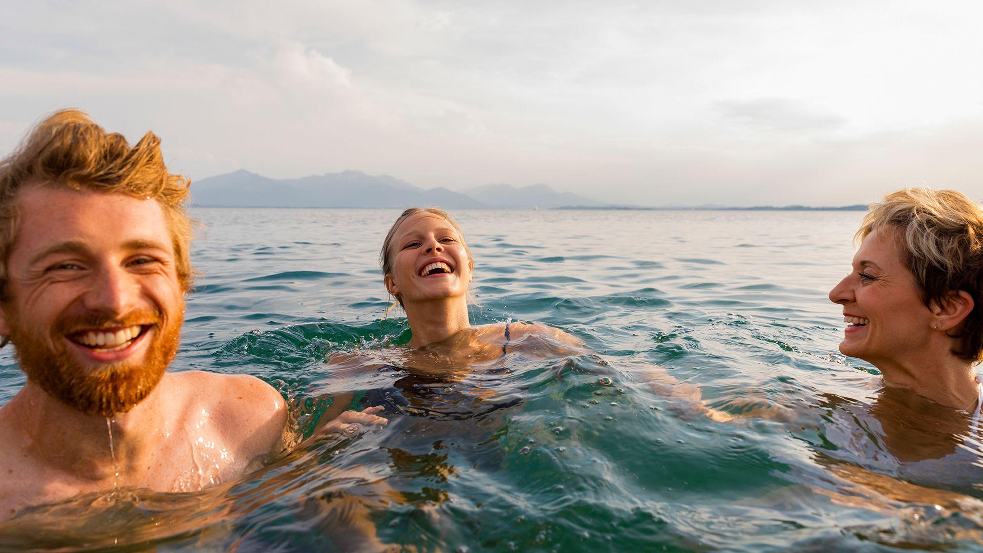 Cheerful young woman splashing water while enjoying swim with friends in sea on sunny day