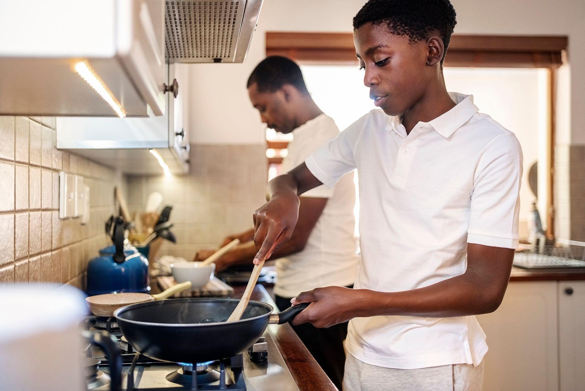Stock photo shows two people, an older person and a younger person, cooking in a kitchen with one of them stirring the contents of a wok on a gas hob.