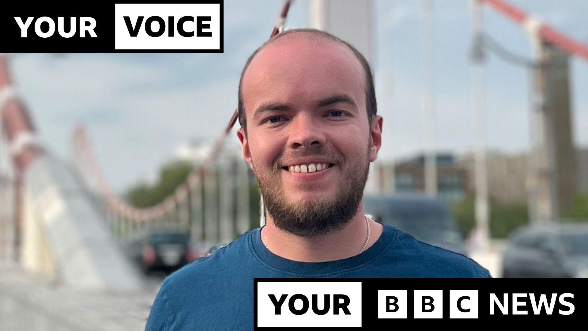 A smiling Lewis Eager, wearing a blue T-shirt, standing on a bridge