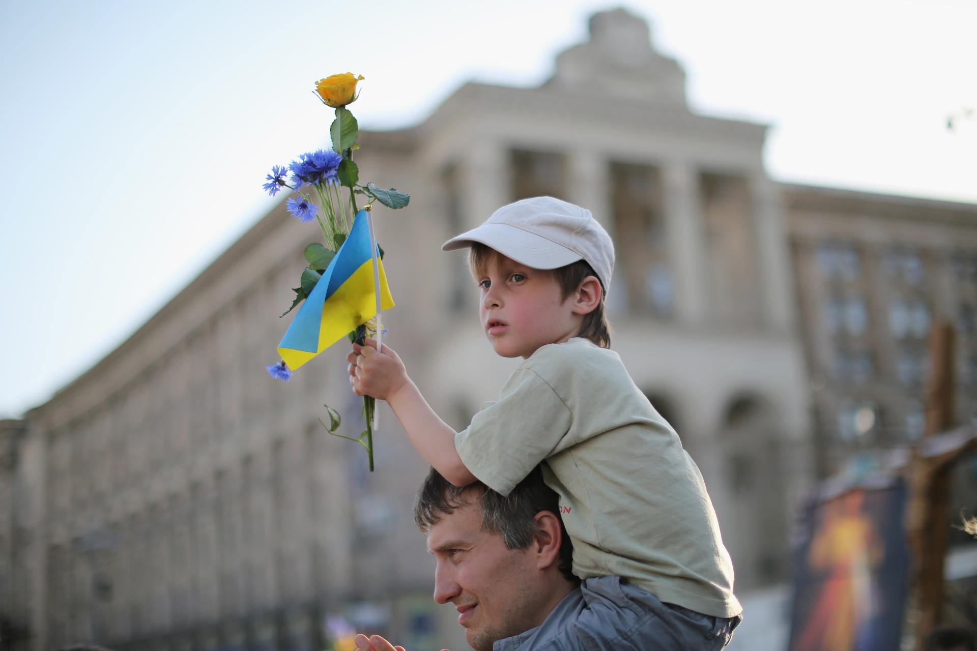 Ukrainian boy on father's shoulders holding a Ukrainian flag and a flower