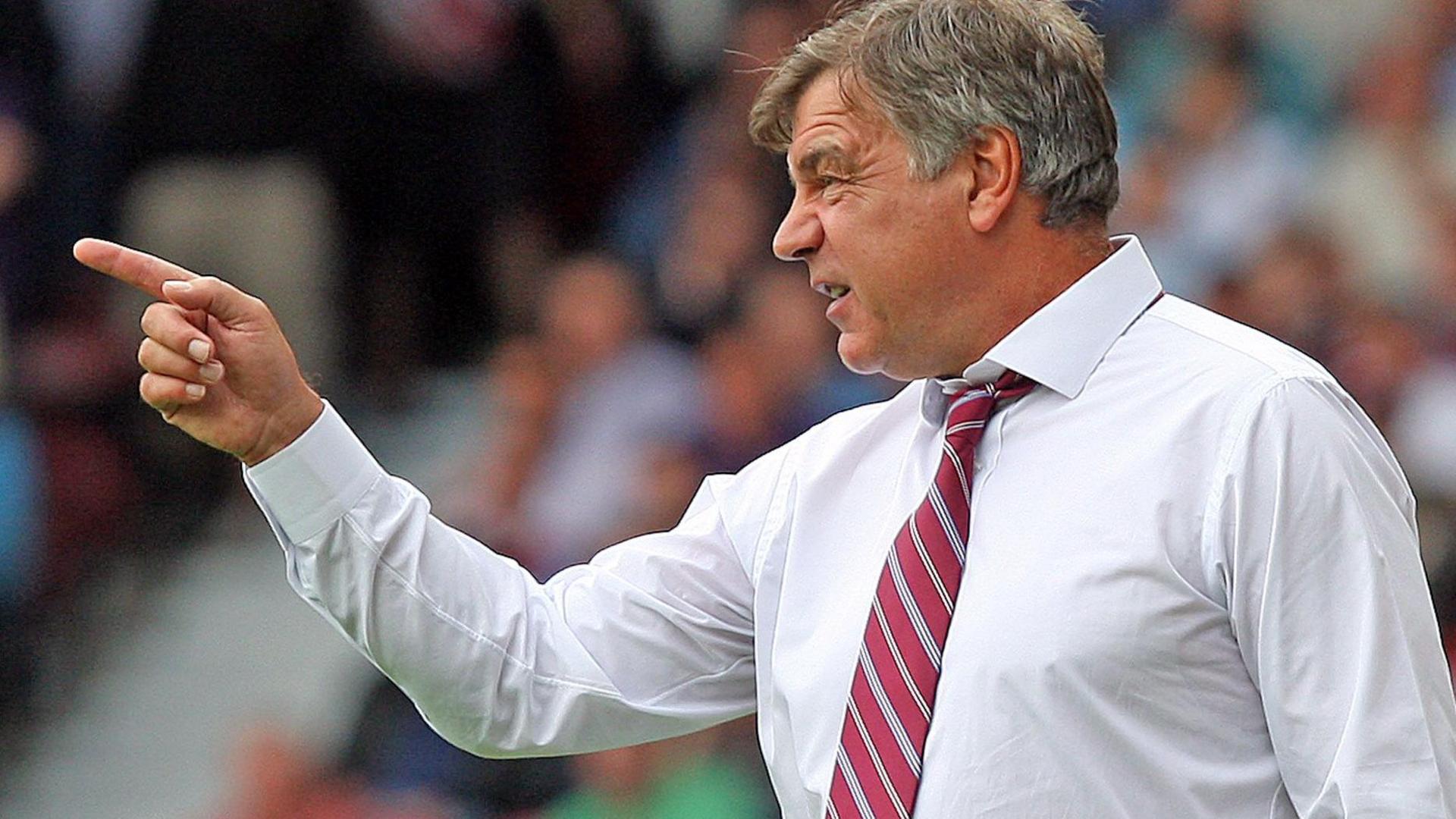 Sam Allardyce wearing a white shirt and claret and blue tie points to his right