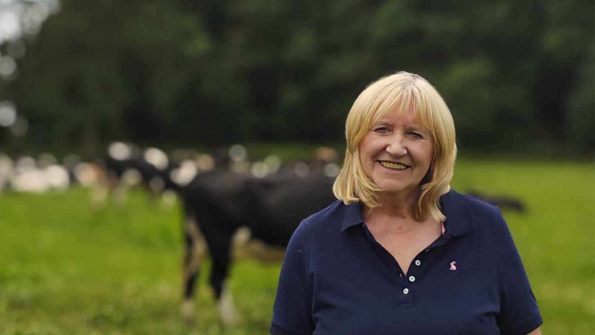 Judy Dilks, a dairy farmer from Derbyshire, standing in a field in front of cows.