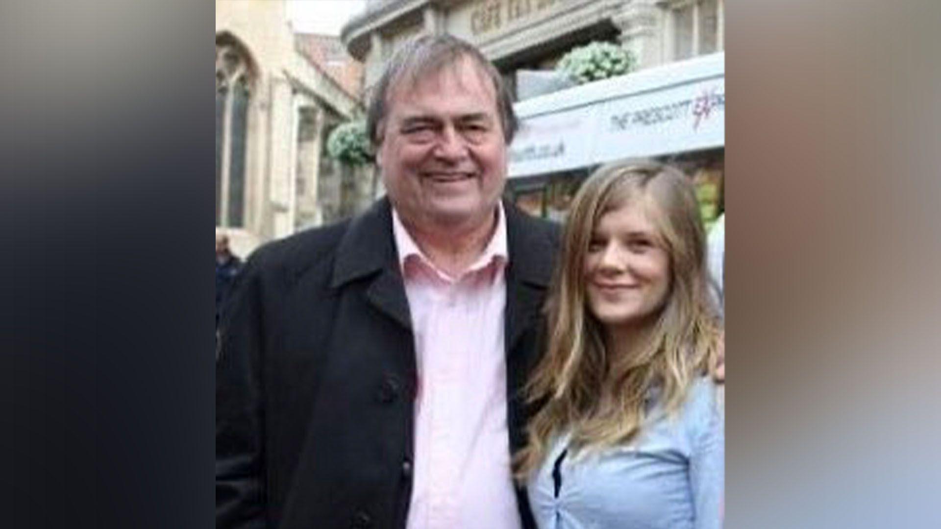 John Prescott, wearing a black suit and pink shirt, stands next to a young Claire Hazelgrove