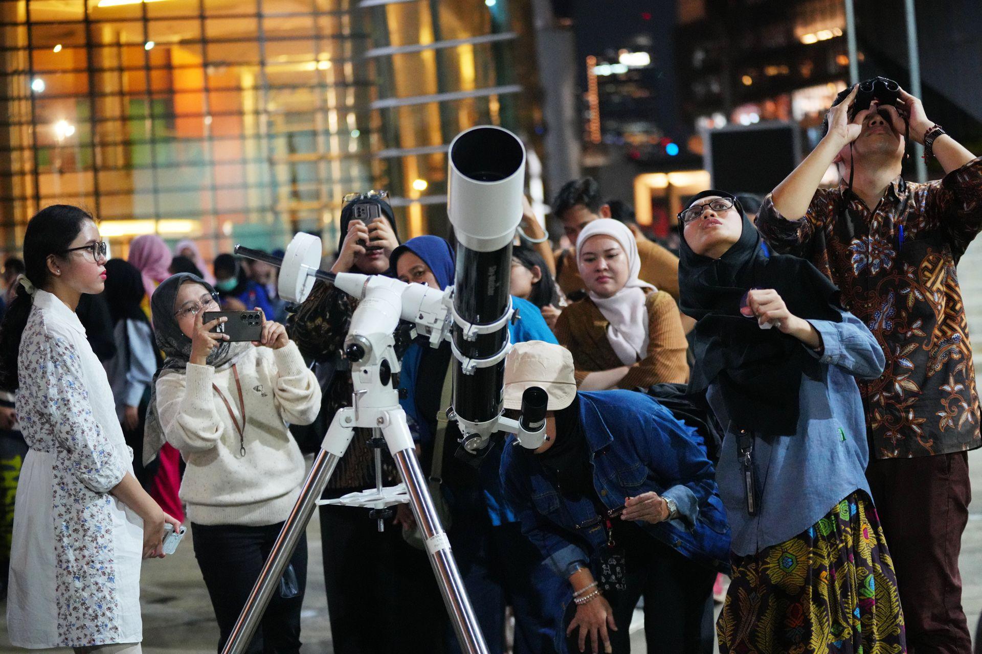 People queue up, some with binoculors or taking photos on their phones, next to a large white telescope in Jakarta on Wednesday.
