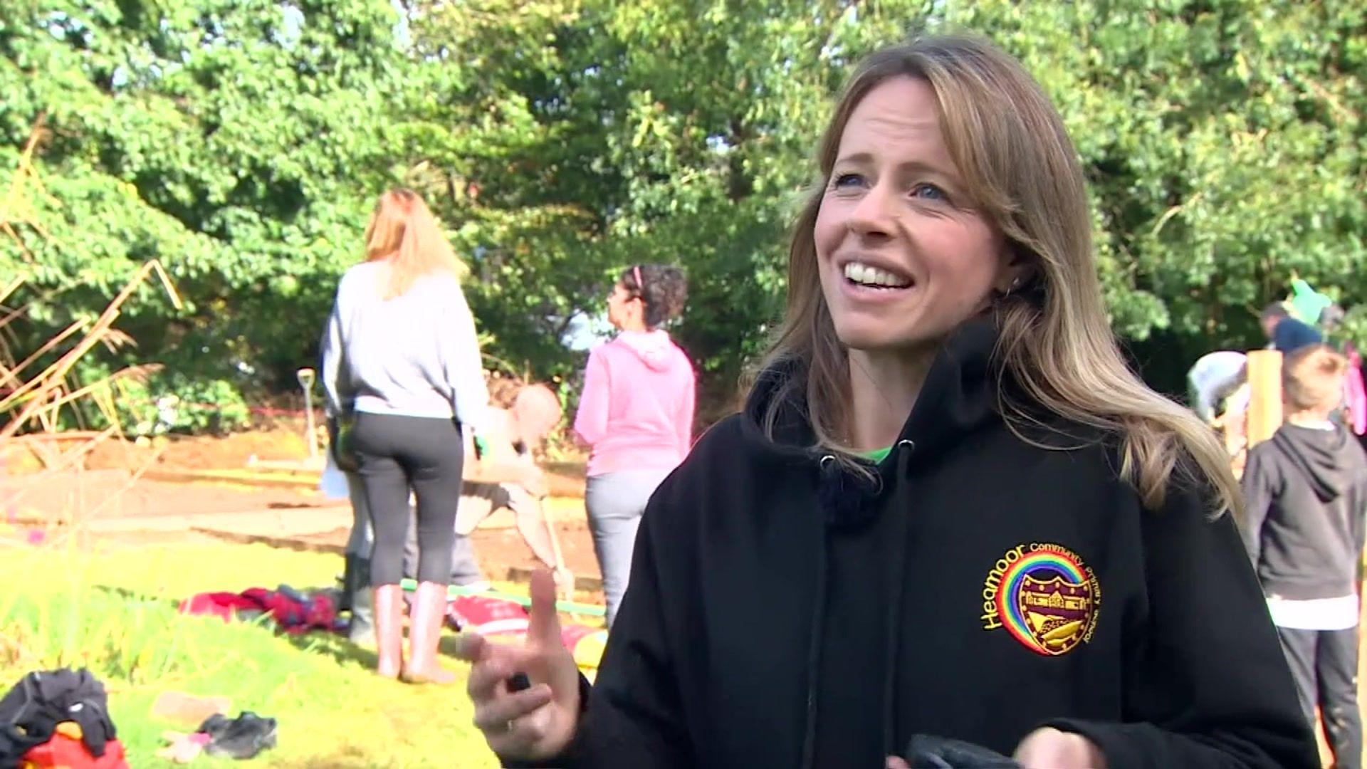 Joanne Bradbury, assistant head teacher, stands to the right wearing a school branded jumper, while in the background children and adults can be seen working the land. 