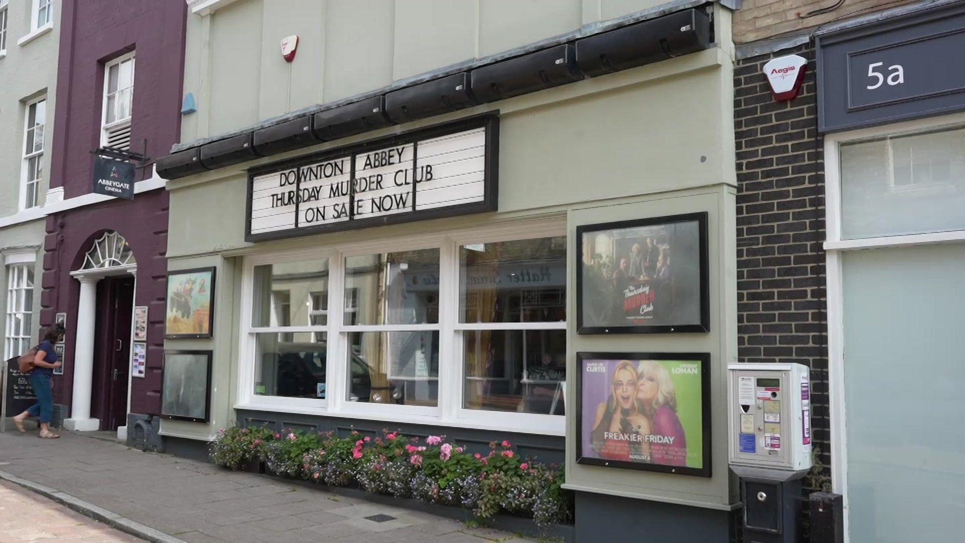 An image taken from the road of the outside of Abbeygate Cinema in Bury St Edmunds. Two movie posts are in frames and a woman is walking inside. 