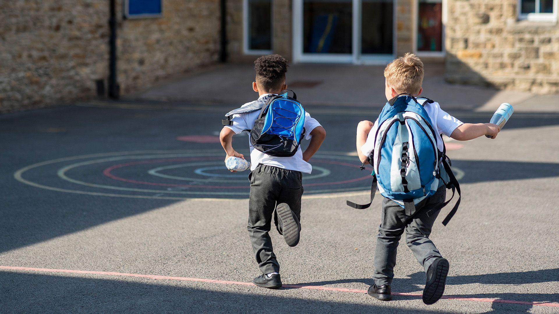 Two boys run into school wearing school uniform and backpacks on their backs