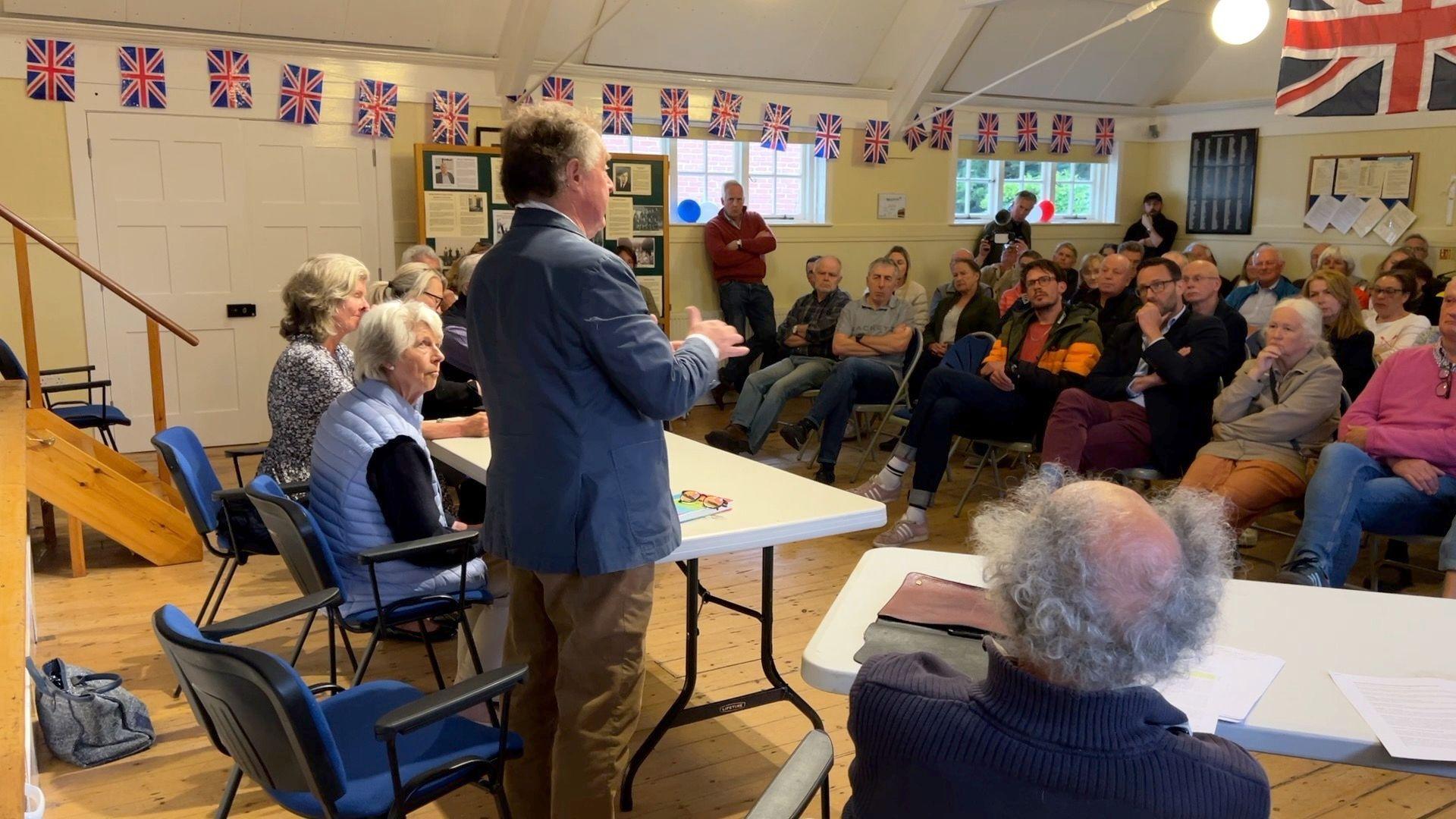 Councillor stands in front of packed village hall parish meeting