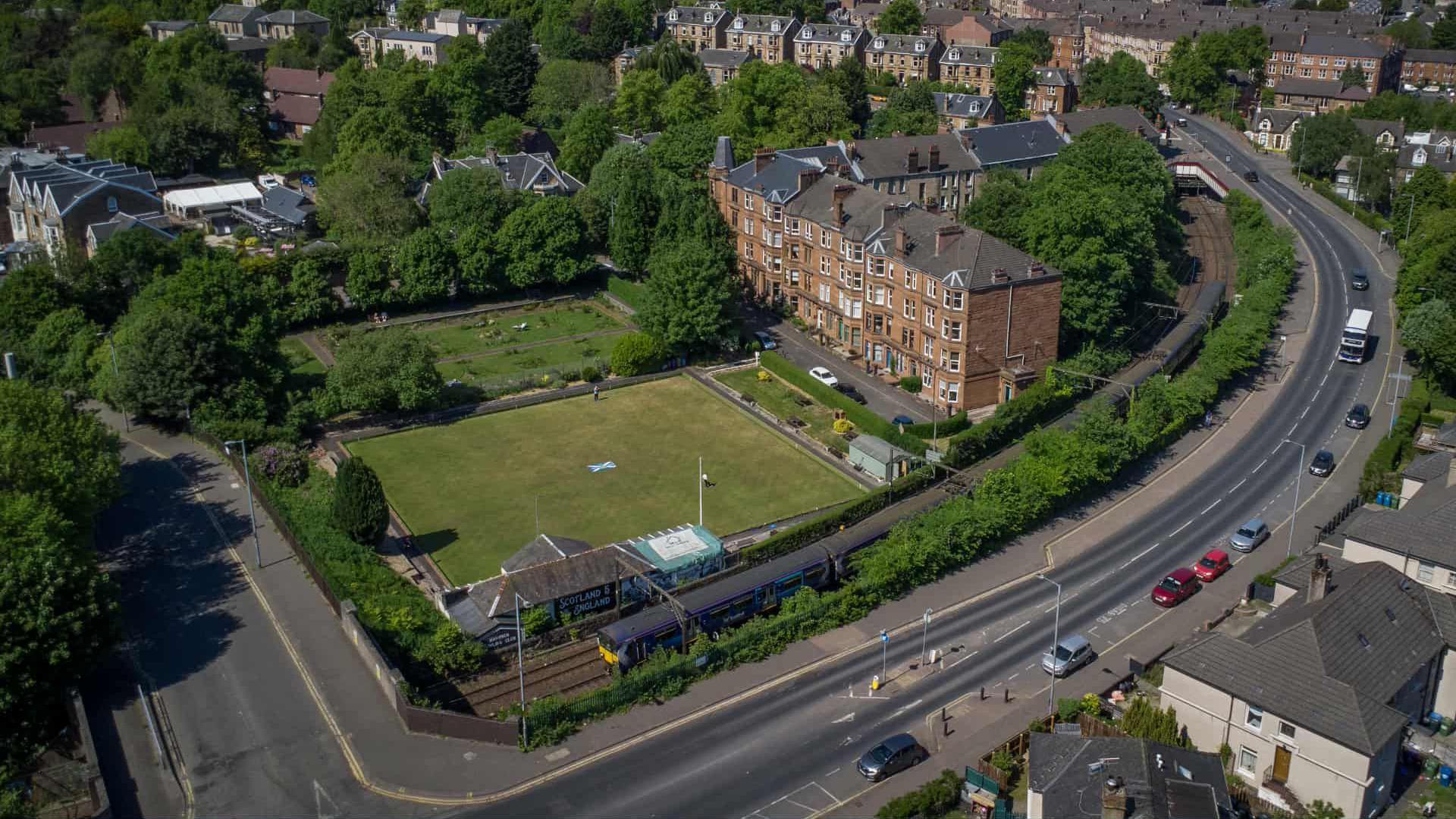 An aerial view of a bowling green with a block of flats and a motorway road running alongside it.