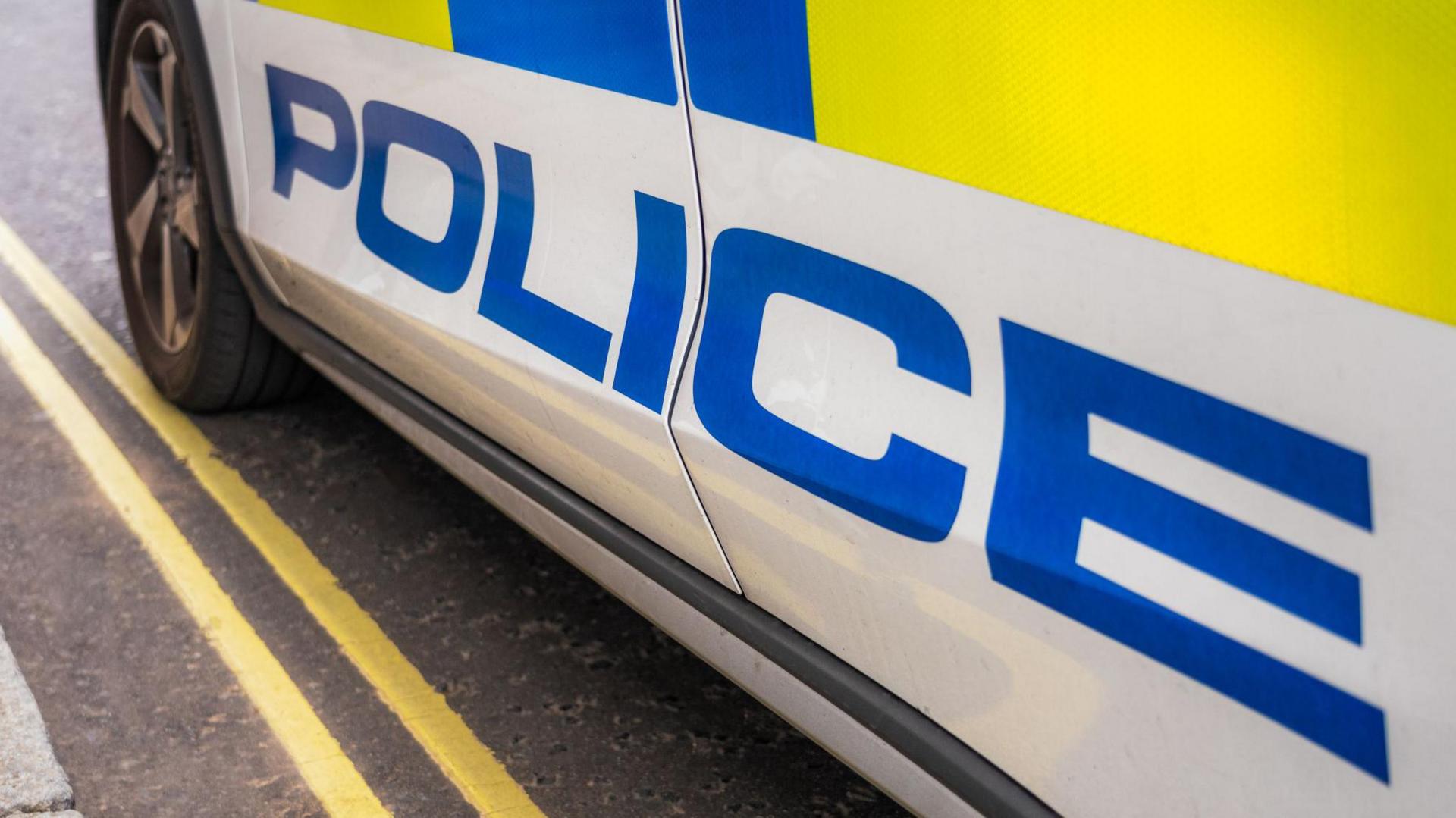 The close-up of the side of a marked police car parked on the side of the road on double yellow lines. 