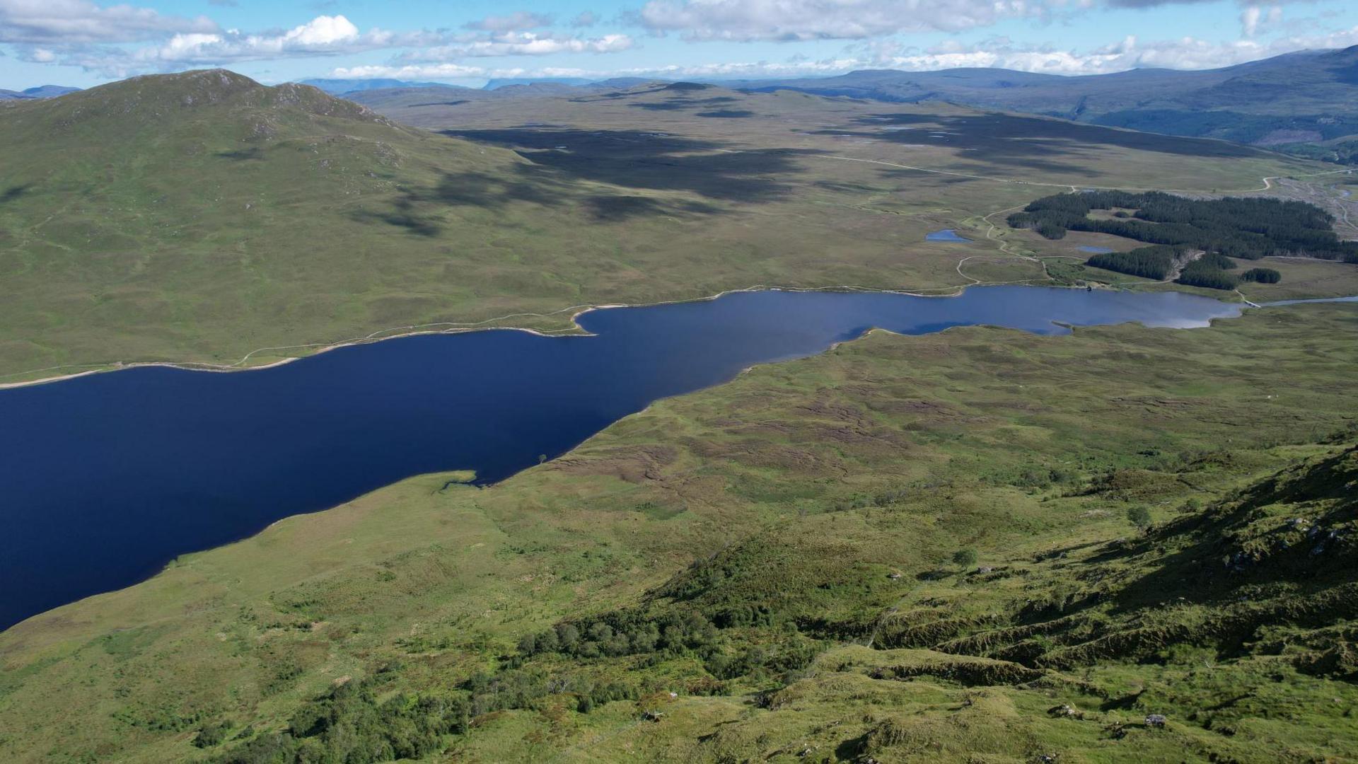 An aerial view of a loch and green hills at Inverbroom.